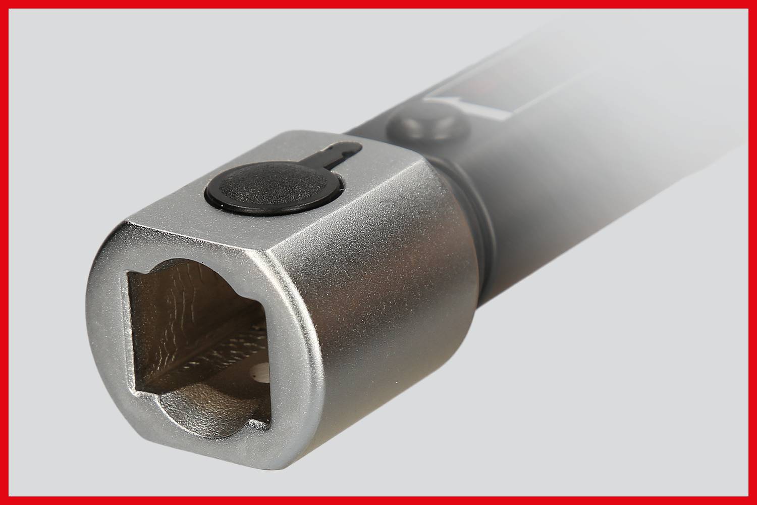 Srebrne narzędzie z kwadratowym zakończeniem, prawdopodobnie klucz dynamometryczny, na szarym tle z czerwoną obwódką.