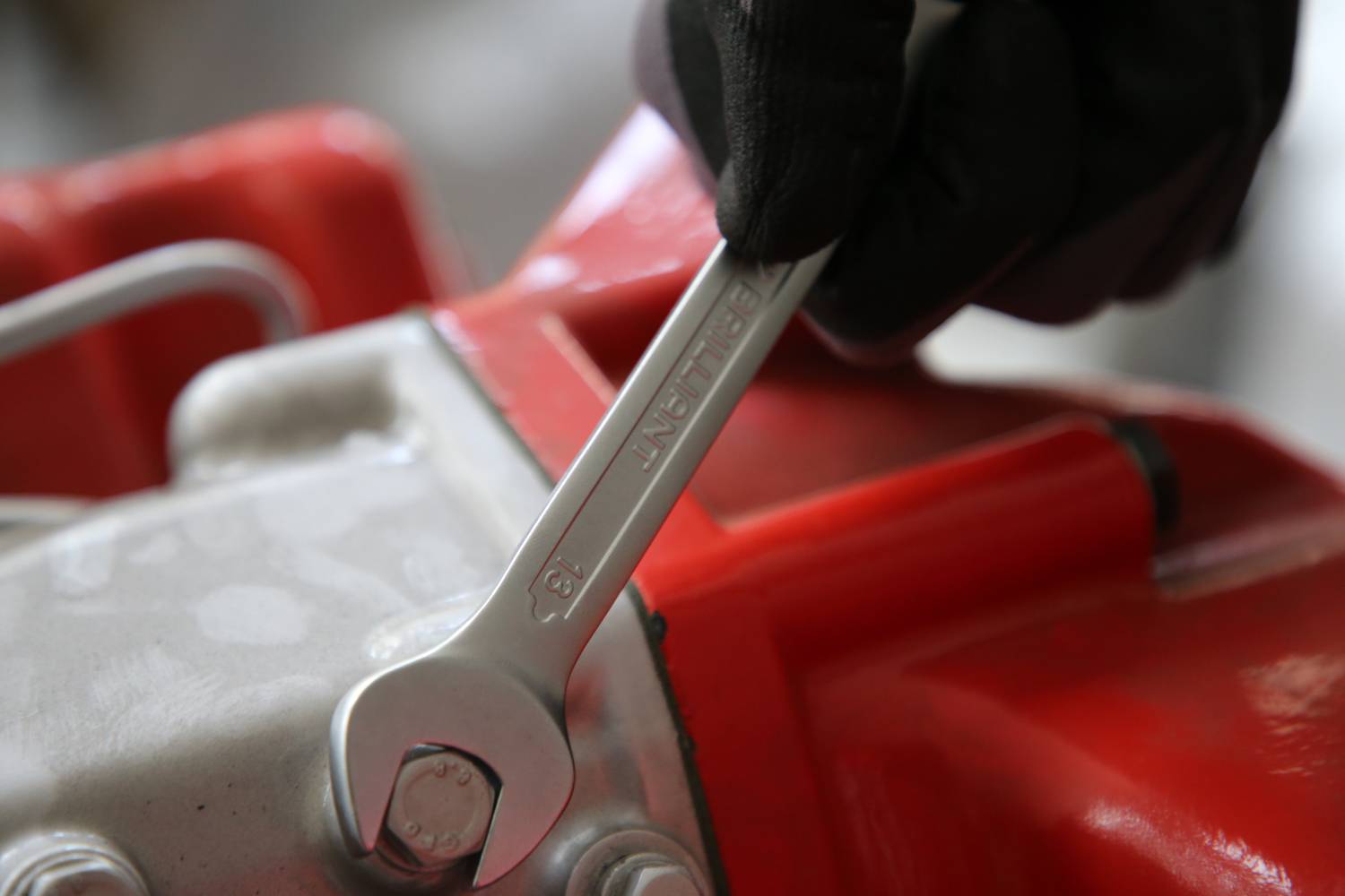 Osoba dokręca śrubę kluczem przy czerwonym urządzeniu mechanicznym.