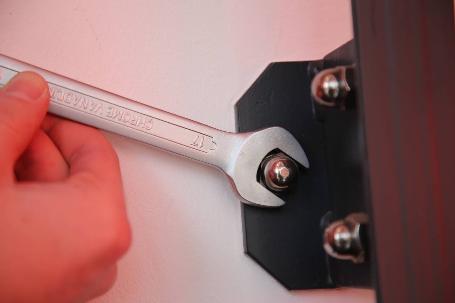 Jedna ręka dokręca nakrętkę na czarnym metalowym wsporniku za pomocą klucza.