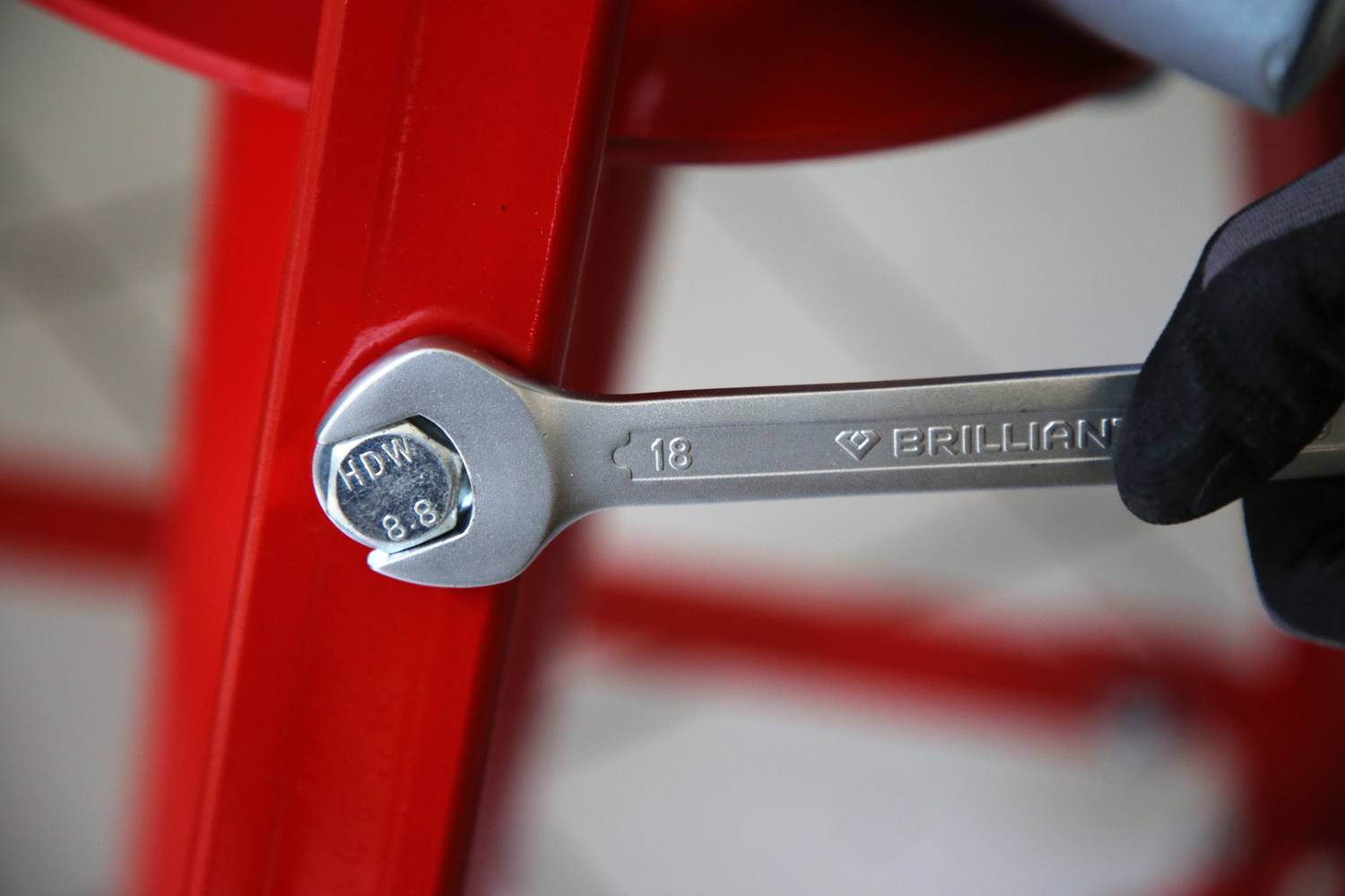Klucz hakowy o rozmiarze 18 jest trzymany w dłoni w rękawiczce, umieszczony obok czerwonej metalowej rury.