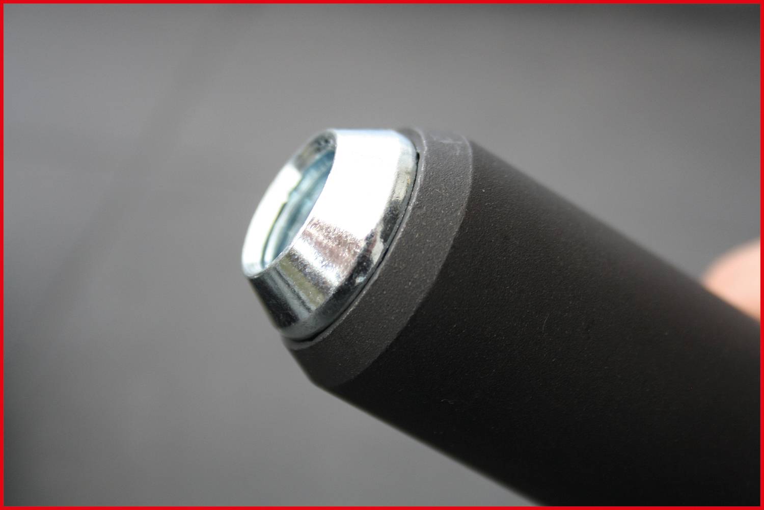 Zbliżenie okrągłej, czarnej metalowej rury z srebrną nakładką na jednym końcu. Ostrość na szczegóły nakładki, rozmyte tło.