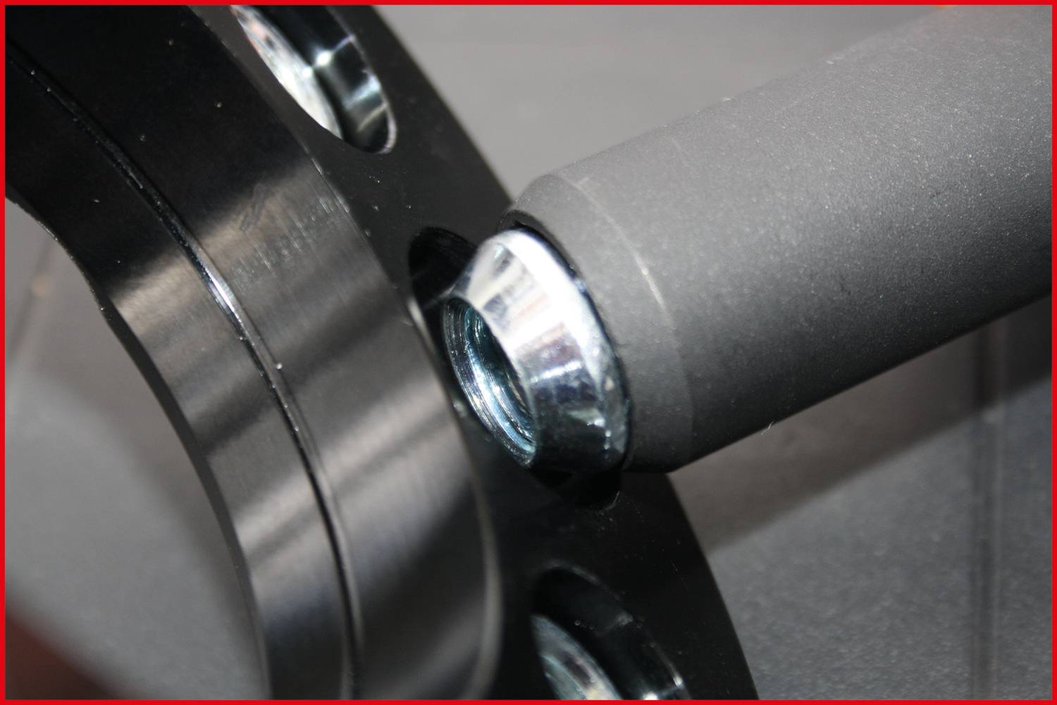 Zbliżenie nakrętki metalowej ze śrubą przymocowanej do czarnej metalowej ramy. Widoczne krawędzie i połączenia śrubowe.