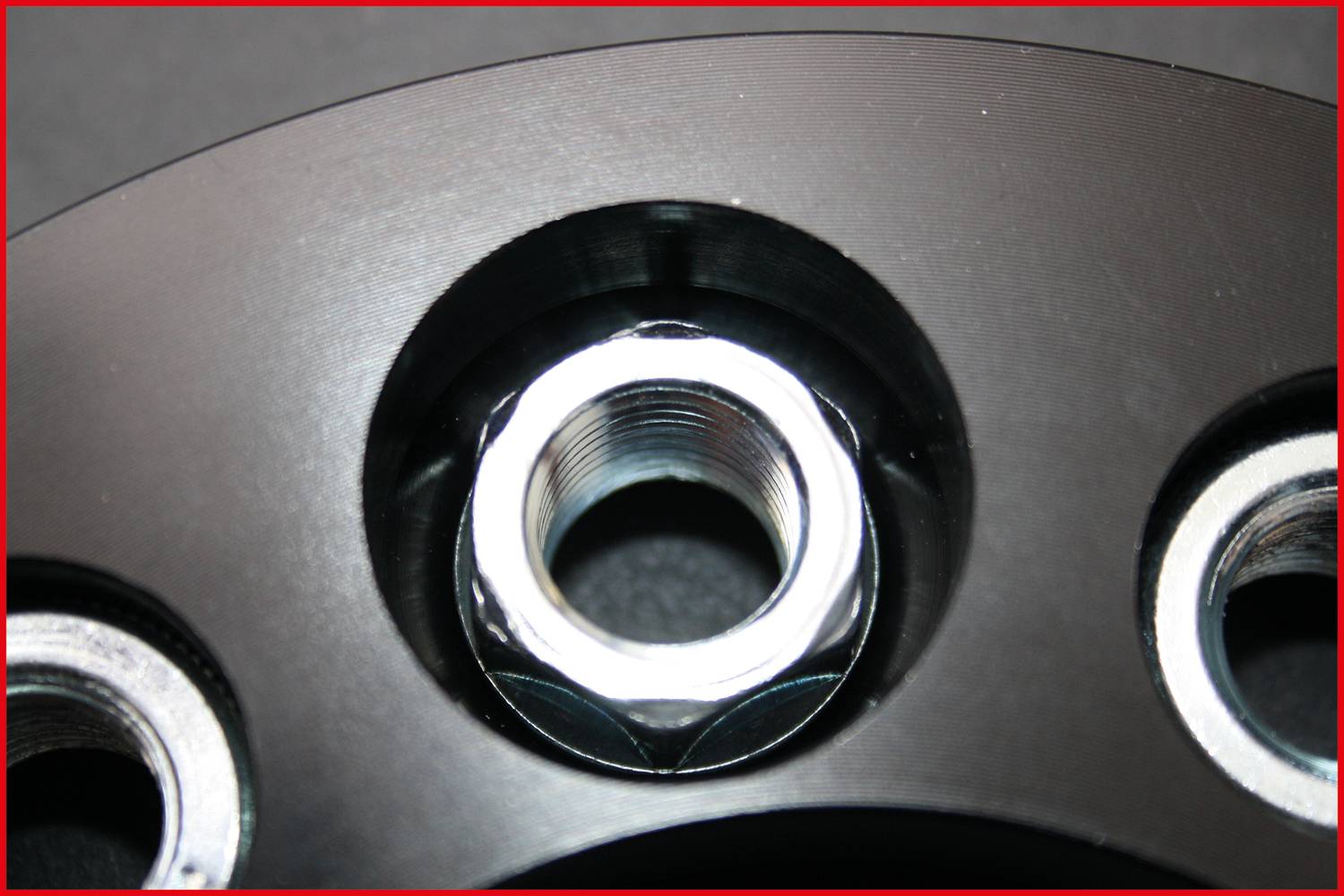 Zbliżenie czarnej metalowej płyty z kilkoma okrągłymi wycięciami i srebrnym gwintem gwintowym w centrum.