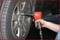 Osoba dokręca nakrętkę koła samochodowego wkrętarką pneumatyczną. Widoczny jest opona.