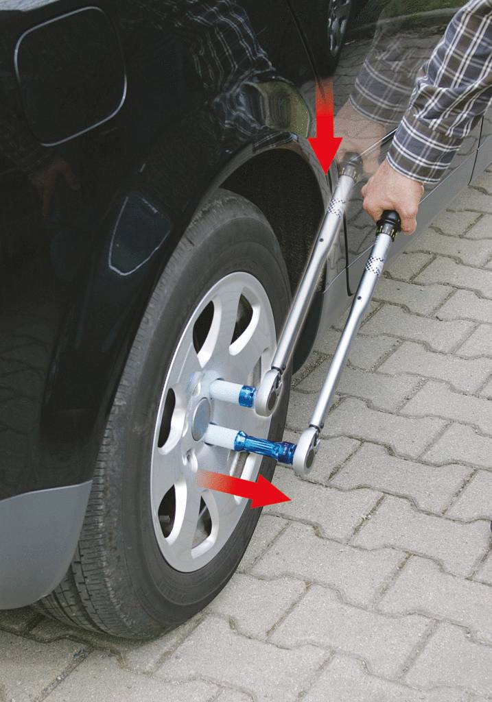 Mężczyzna dokręca nakrętki kół samochodu za pomocą dwóch kluczy krzyżowych.