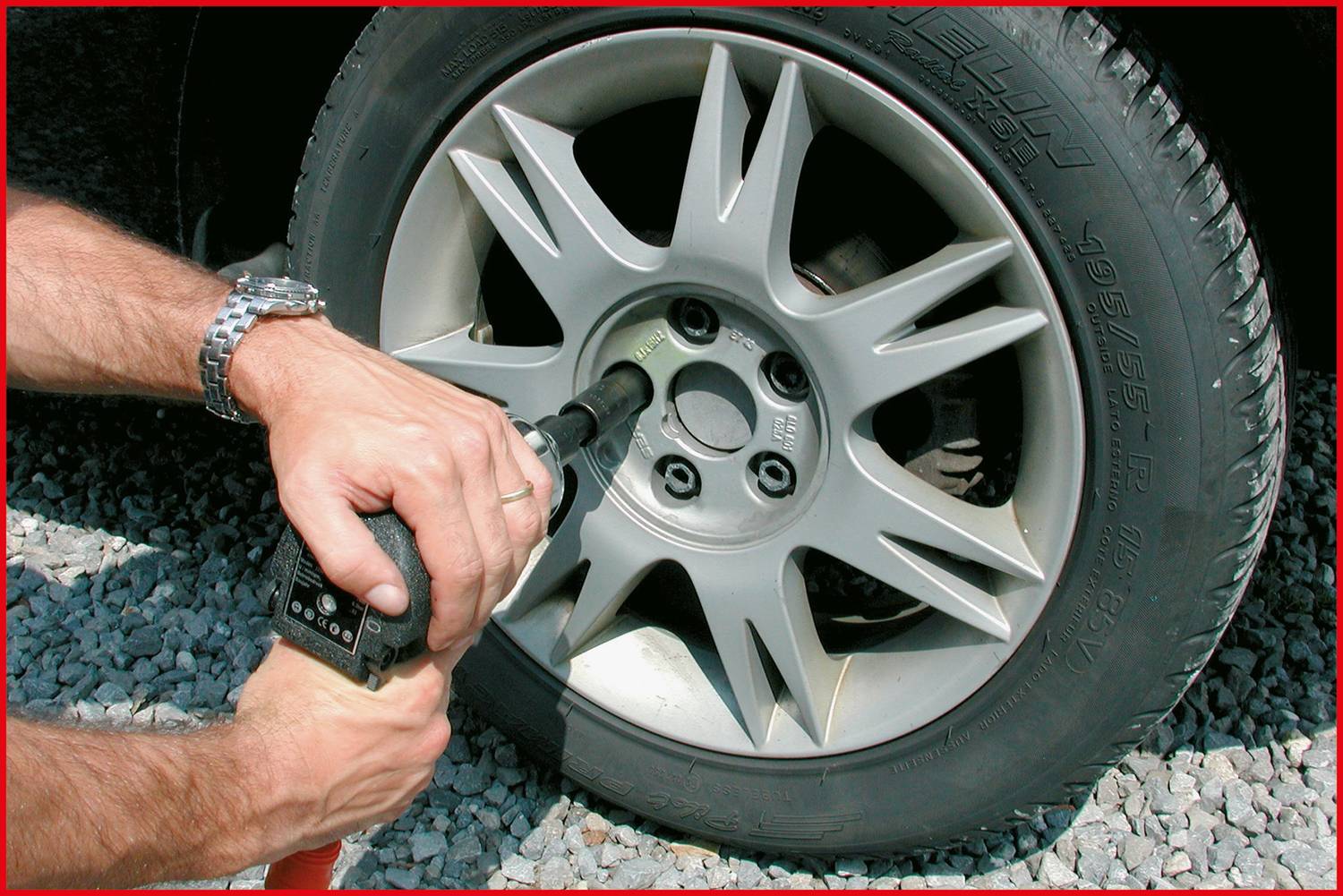 Osoba wymienia oponę w samochodzie, odkręcając śruby koła za pomocą klucza udarowego.