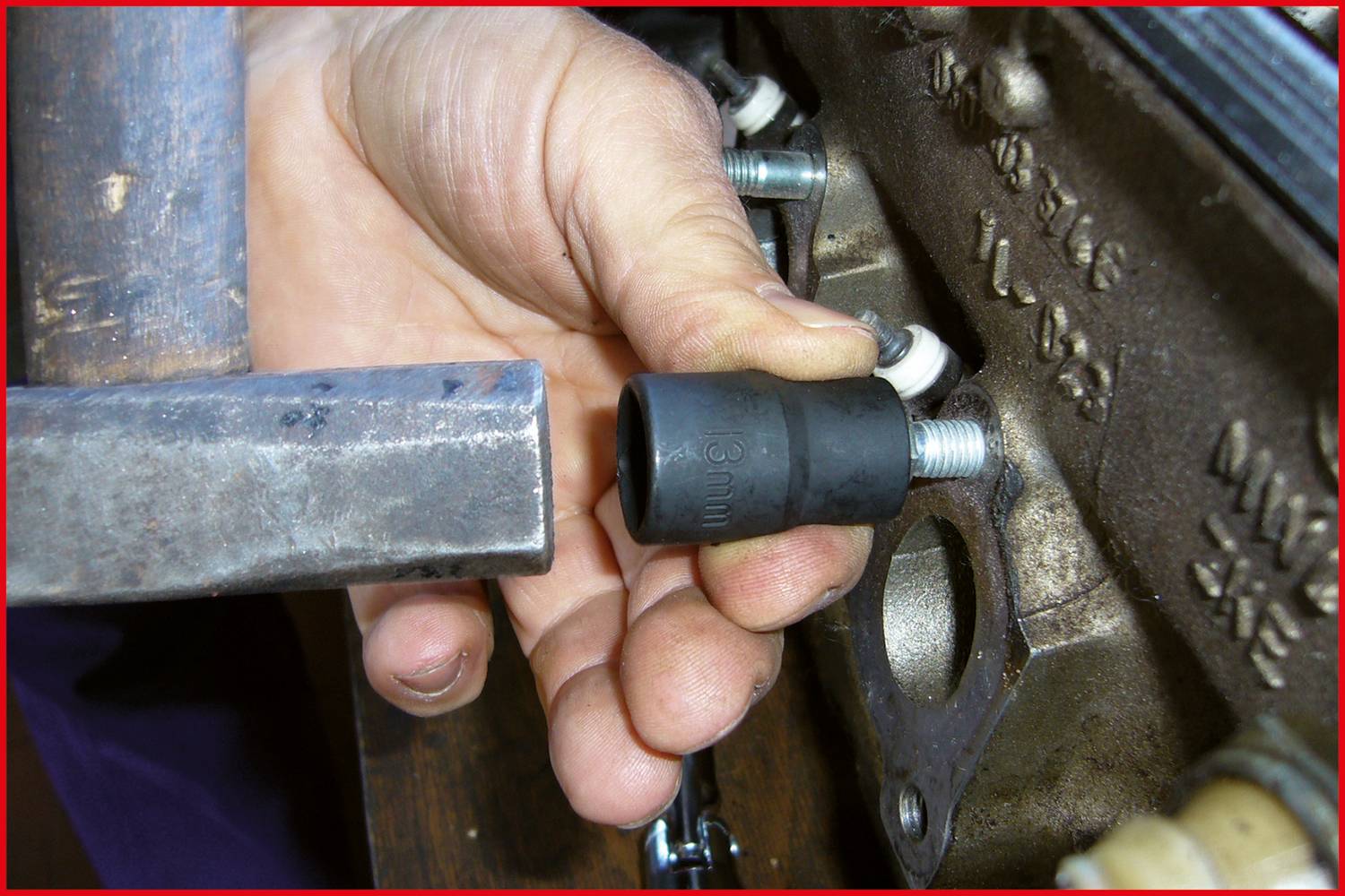 Jedna ręka trzyma czarną gumową nasadkę na elemencie maszyny, prawdopodobnie w celu zakrycia lub zabezpieczenia połączenia śrubowego.