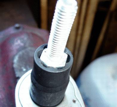 Zbliżenie klucza do nakrętek, który dokręca długą śrubę. Tło jest rozmyte.