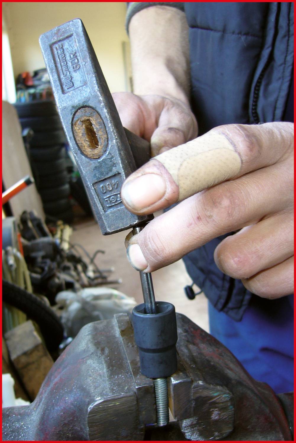 Jedna ręka trzyma metalową pieczęć, podczas gdy kciuk w opasce przytrzymuje imadło do obróbki metalu lub drewna.