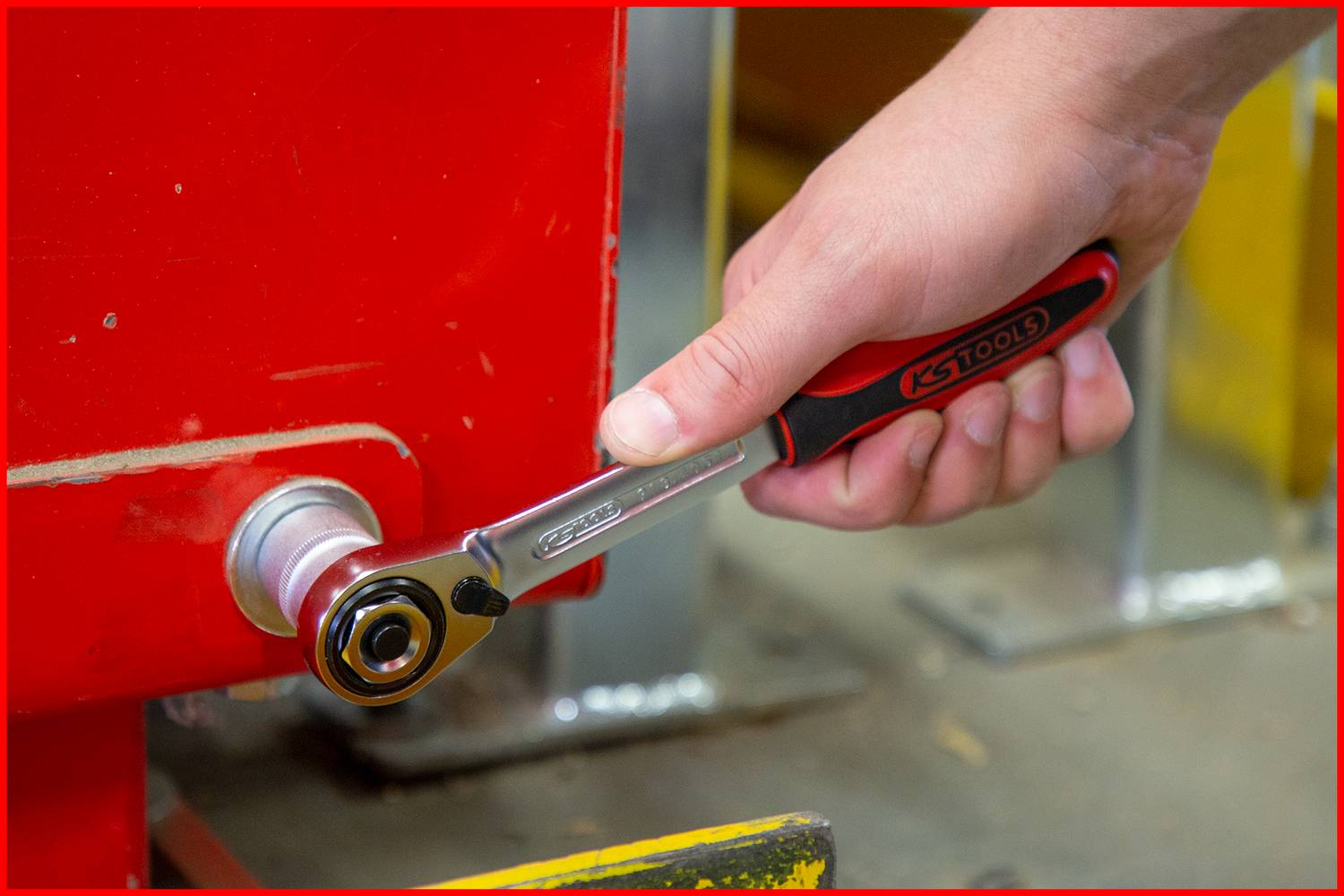 Dłoń trzyma grzechotkę, która dokręca śrubę na czerwonej powierzchni. Zbliżenie na obsługę narzędzia.