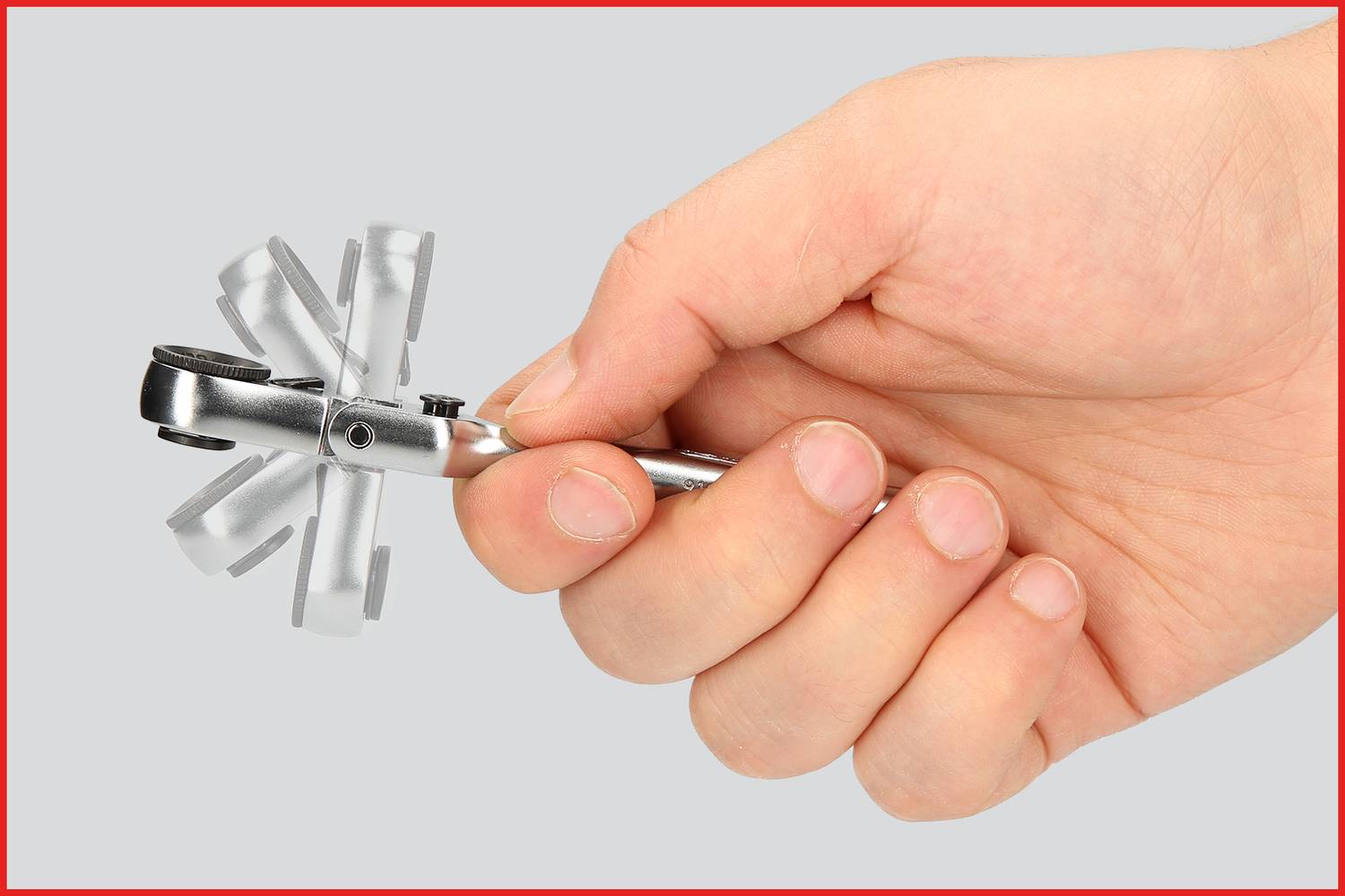 Zbliżenie dłoni trzymającej mały, srebrny klucz nastawny. Tło jest jednorodne szare.