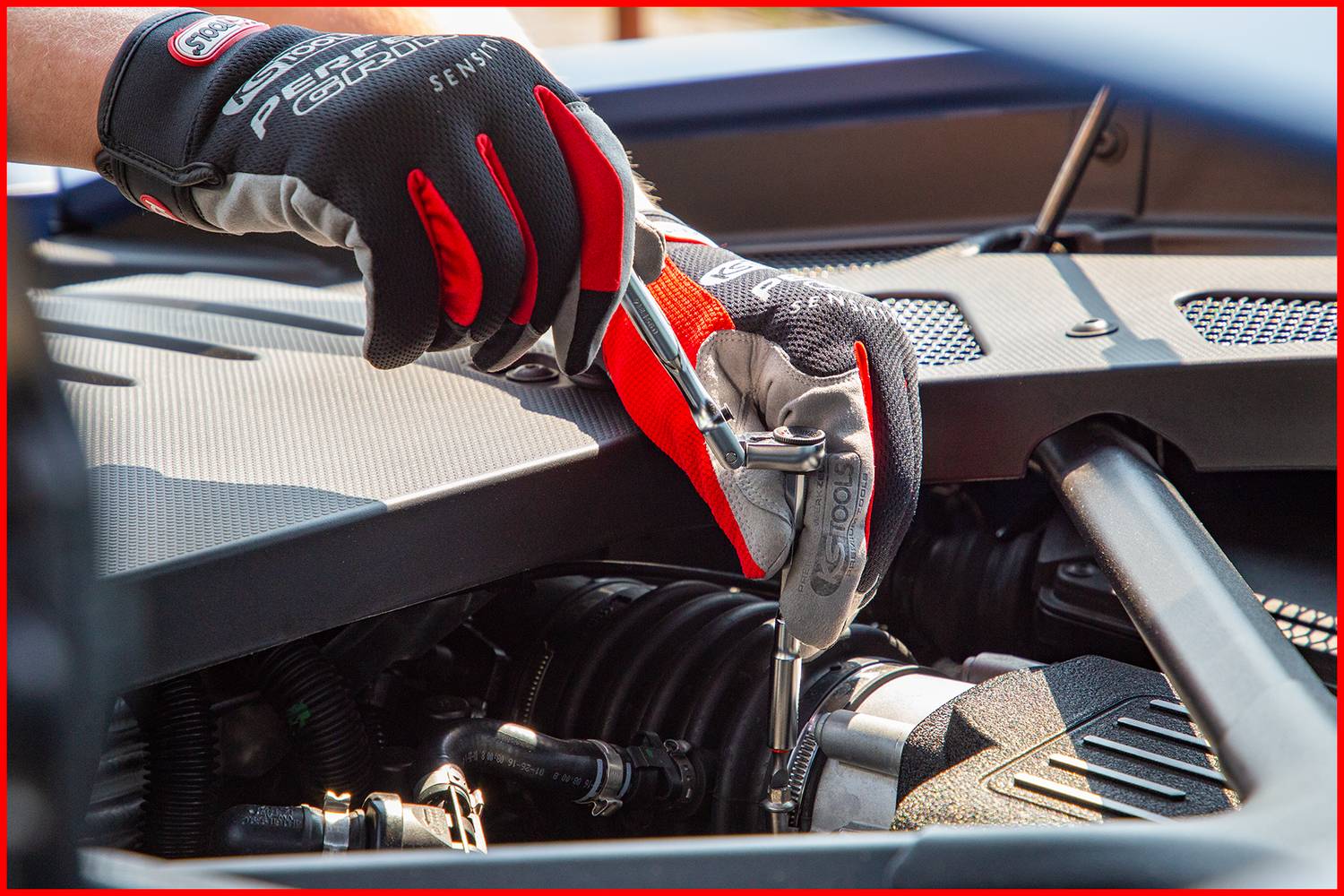 Osoba w rękawiczkach dokręca śrubę kluczem w otwartej komorze silnika pojazdu.