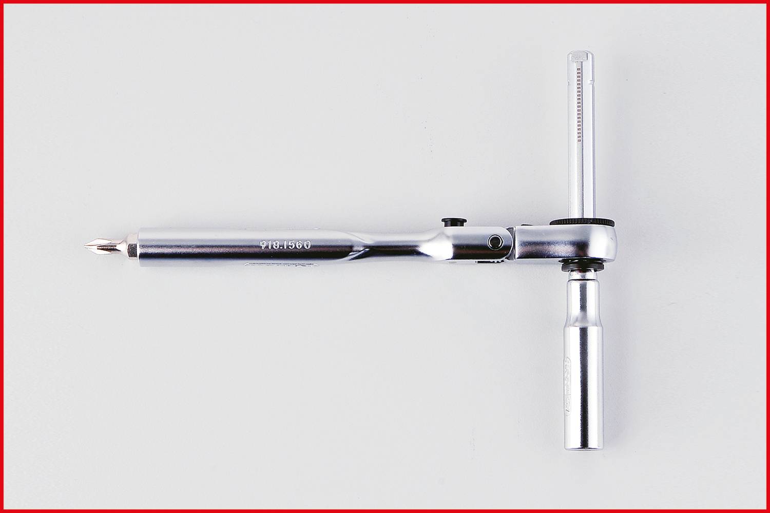 Wkrętak z wymiennymi grotami leży na jasnym tle. Uchwyт jest cylindryczny i metalowy.