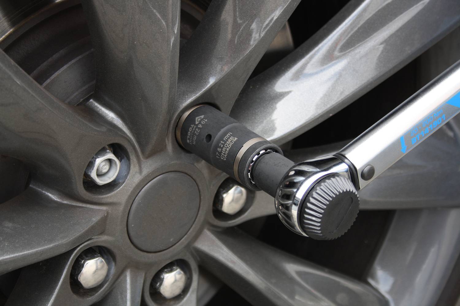 Zbliżenie opony samochodu dokręcanej kluczem dynamometrycznym. Klucz jest nasadzony na nakrętkę koła.