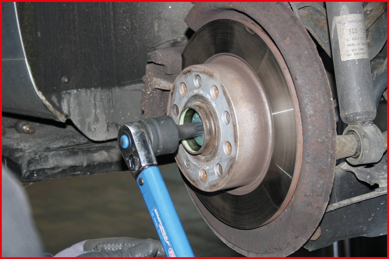 Mechanik dokręca śrubę na tarczy hamulcowej samochodu za pomocą klucza dynamometrycznego.