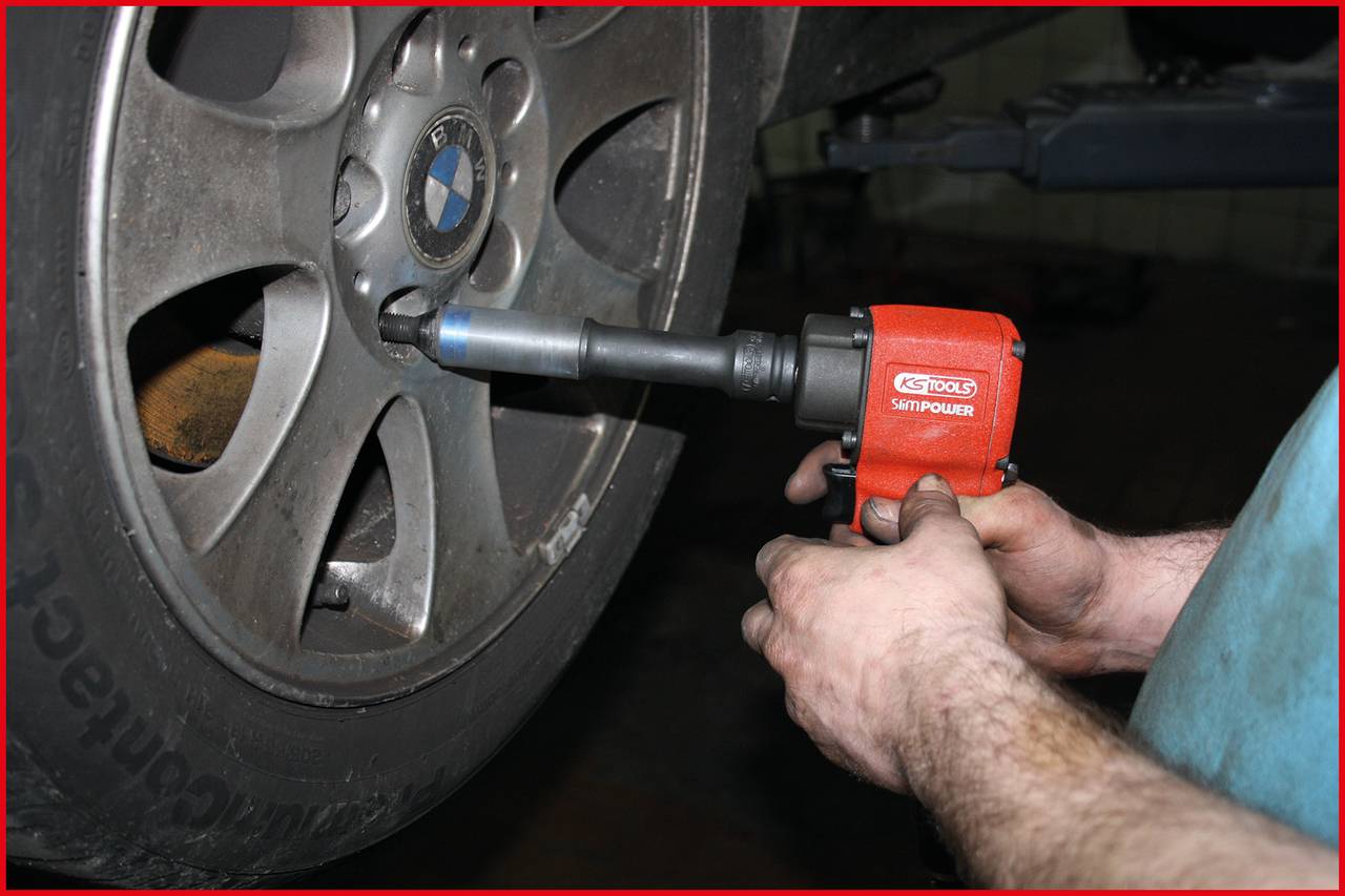 Mechanik dokręca nakrętkę koła samochodu kluczem udarowym.