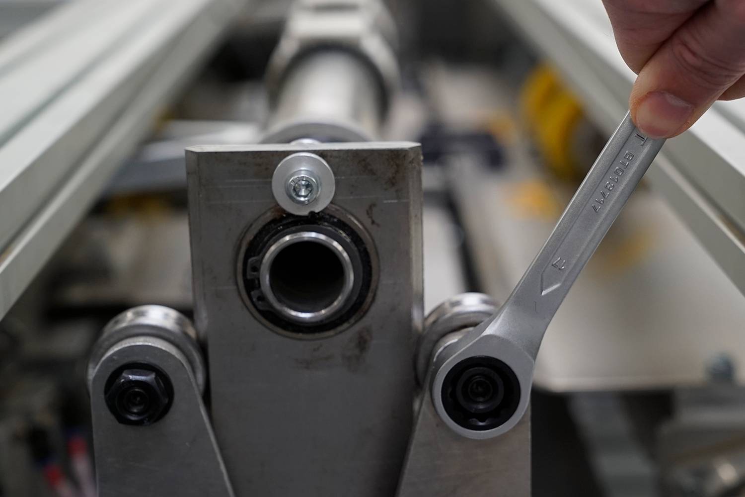 Ręka dokręca śrubę kluczem na metalowej maszynie. Nacisk położony jest na użycie narzędzia.