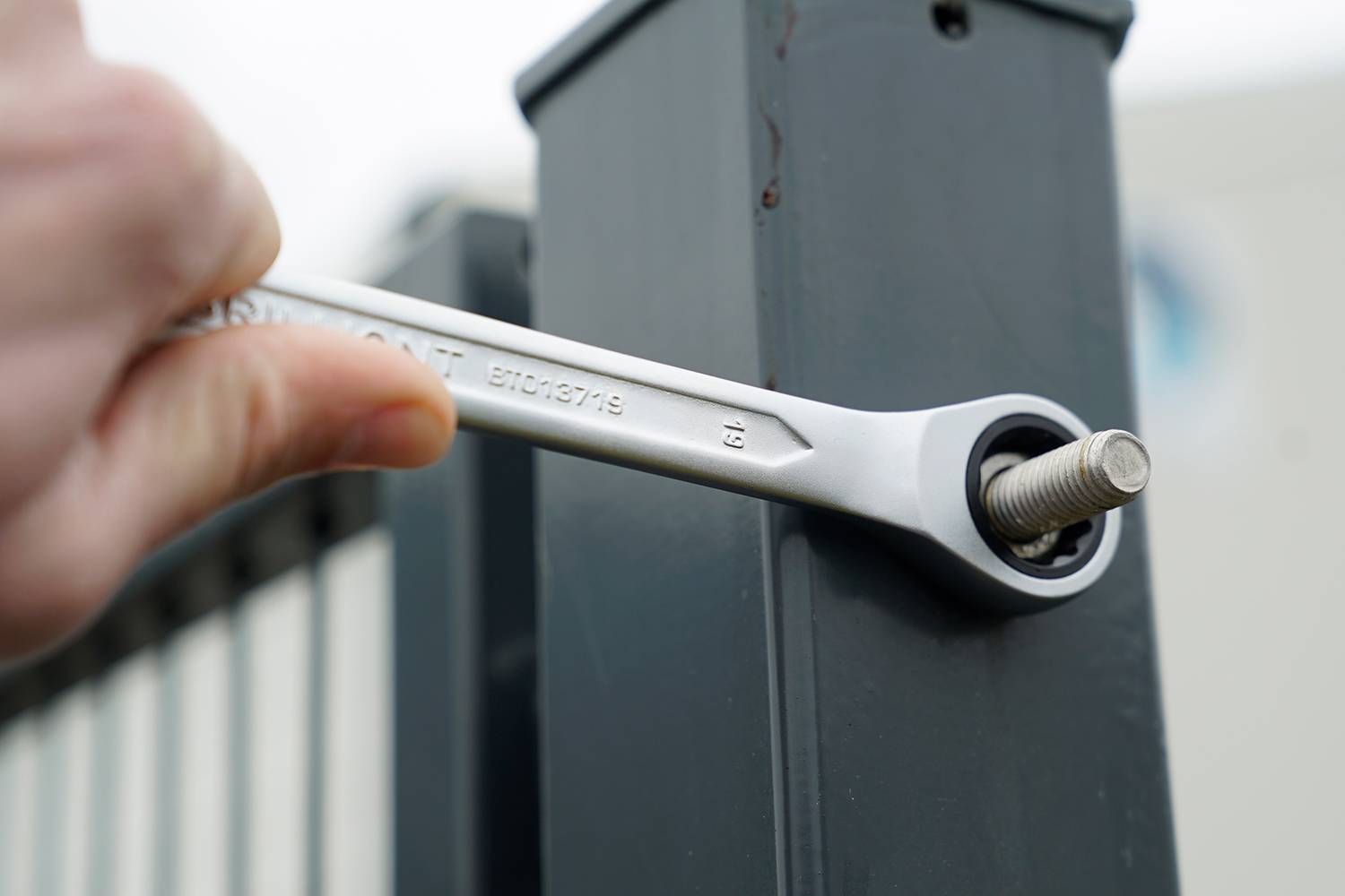 Dłoń dokręca śrubę kluczem na metalowym słupie.
