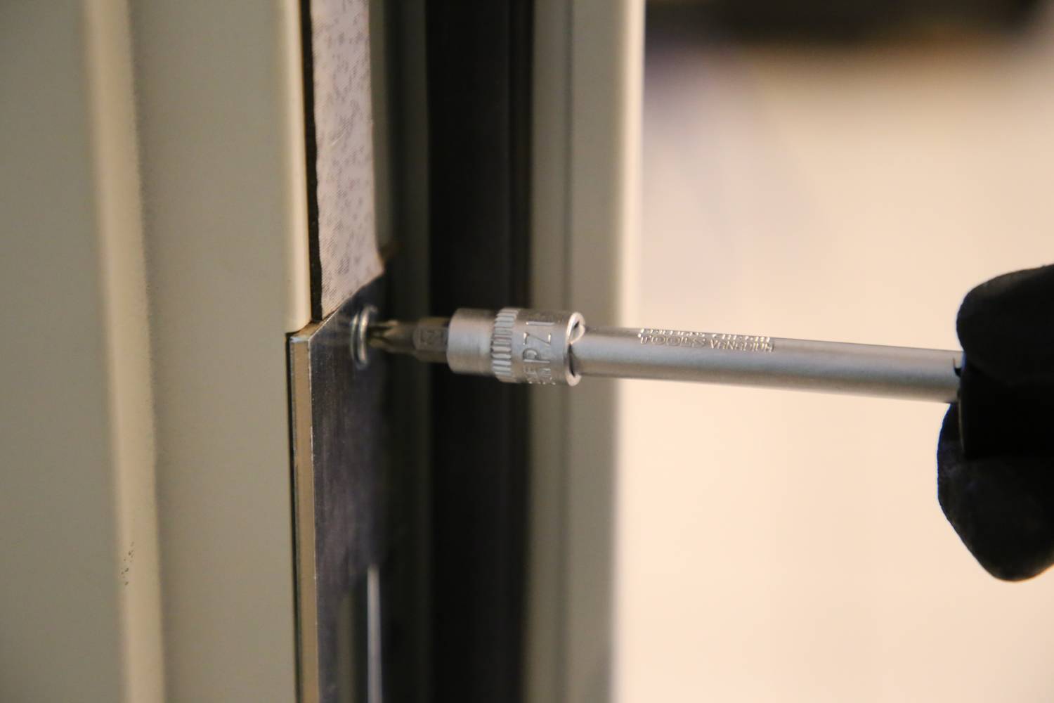 Osoba dokręca wkrętakiem śrubę w framudze drzwiowej, prawdopodobnie podczas instalacji lub naprawy.