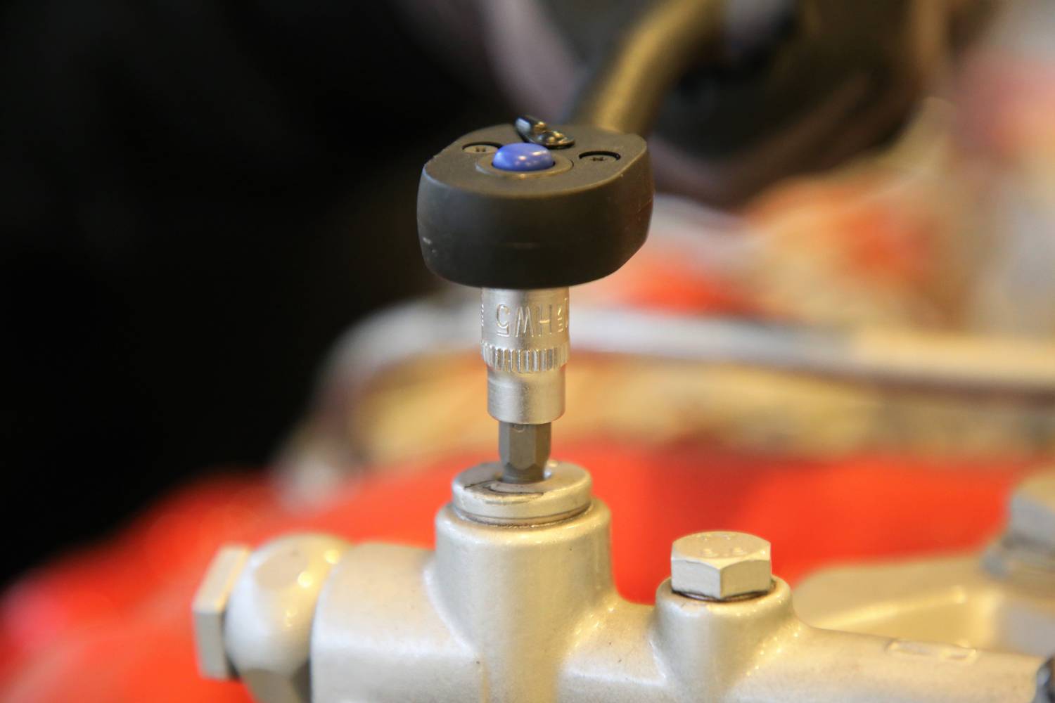 Zbliżenie klucza dynamometrycznego używanego przy kole samochodowym. Na tle widoczna jest ręka regulująca narzędzie.