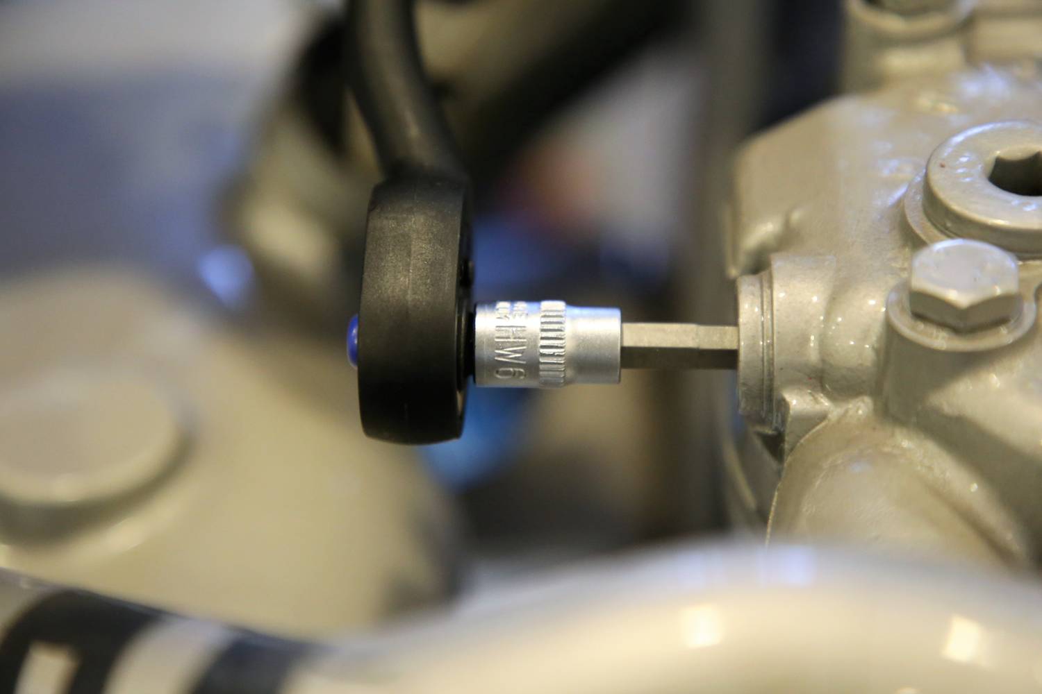 Zbliżenie metalowego zaworu na części maszyny lub pojazdu z czarnym przewodem i śrubą w tle.