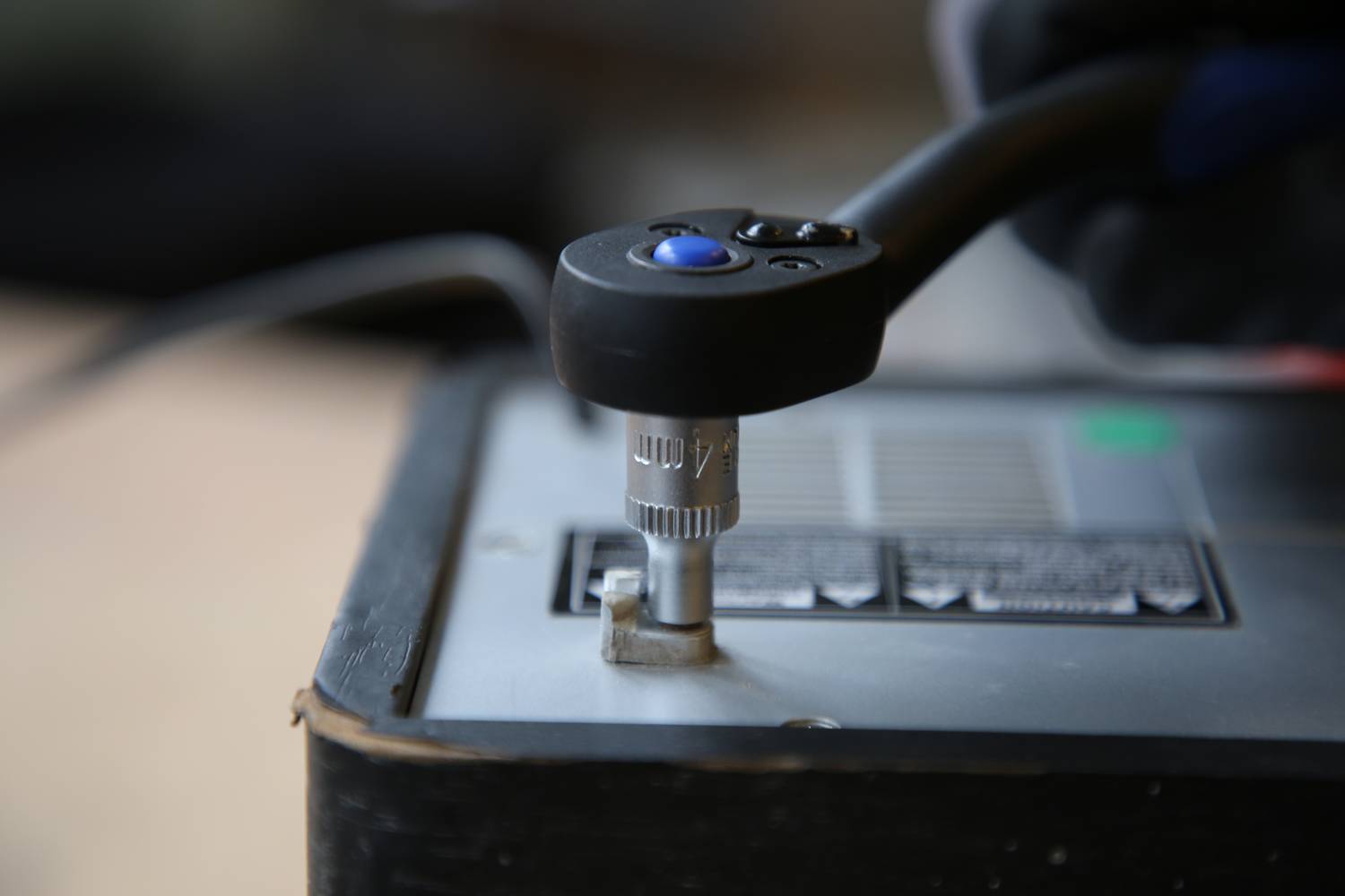 Jedna ręka trzyma klucz hydrauliczny, dokręcając śrubę przy baterii. Fokus jest na procesie pracy.