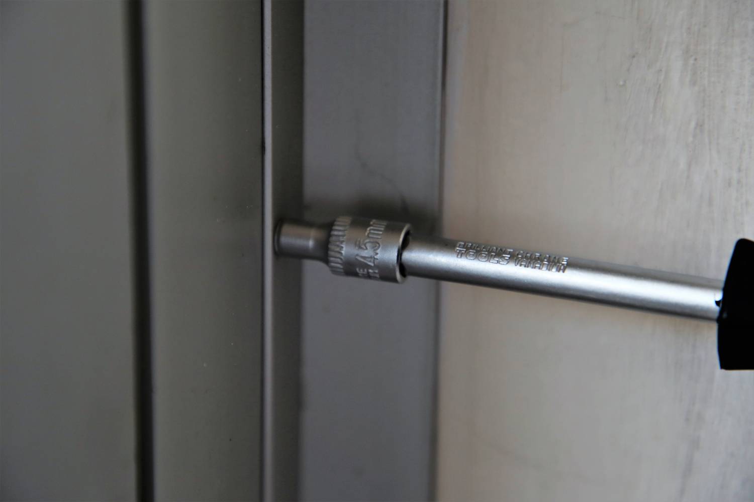 Srebrny klucz do śrub wkręca śrubę w płytkę metalową.