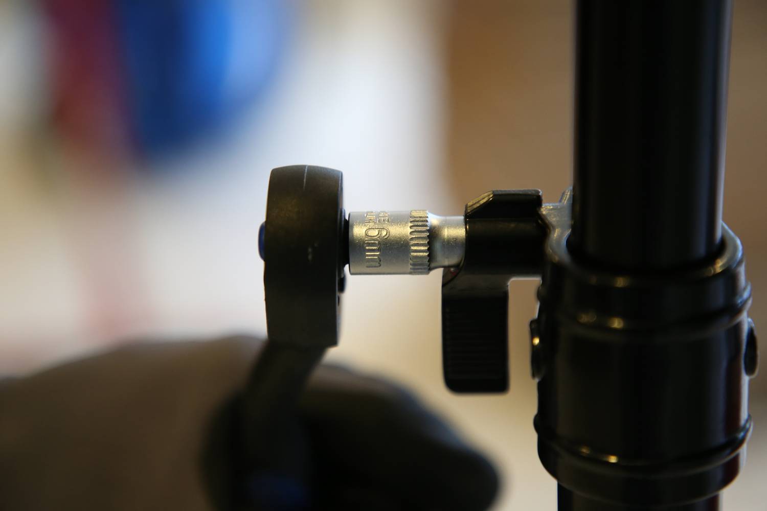 Osoba przekręca przełącznik na statywie, fokus na pokrętło regulacyjne na pierwszym planie. Tło jest rozmyte.