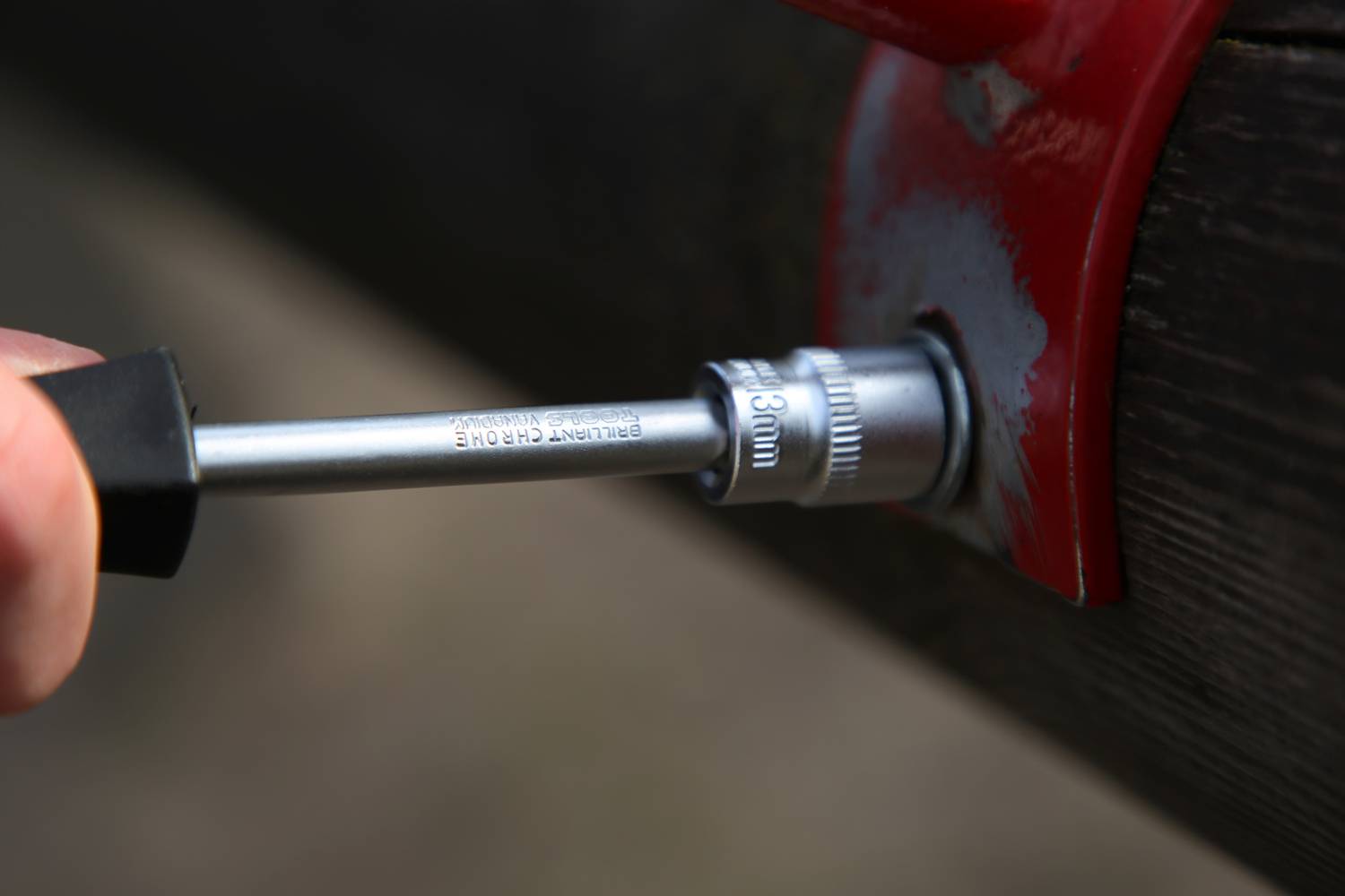 Metalowy rurociąg jest dokręcany kluczem nasadowym. Nakładka wskazuje '20mm'. Czerwony uchwyt znajduje się na rurze.