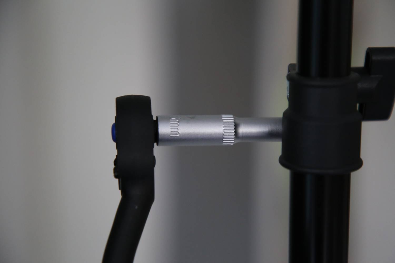 Czarny mikrofonowy wysięgnik z srebrnym, regulowanym przegubem jest zamontowany na statywie i umieszczony przed neutralnym tłem.