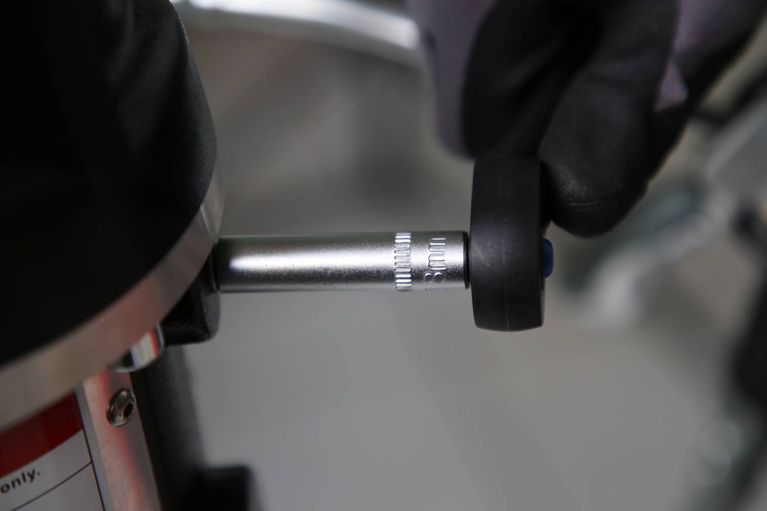 Rękawica obraca srebrny pokrętło na urządzeniu, na którym widoczne są delikatne oznaczenia.