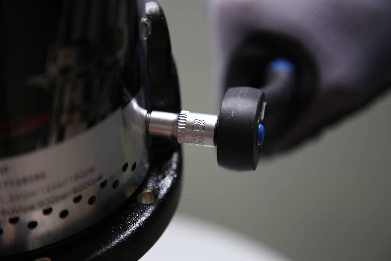 Zbliżenie narzędzia z pokrętłem trzymanym przez dłoń w rękawiczce. Ostrość obrazu skupiona jest na pokrętle.