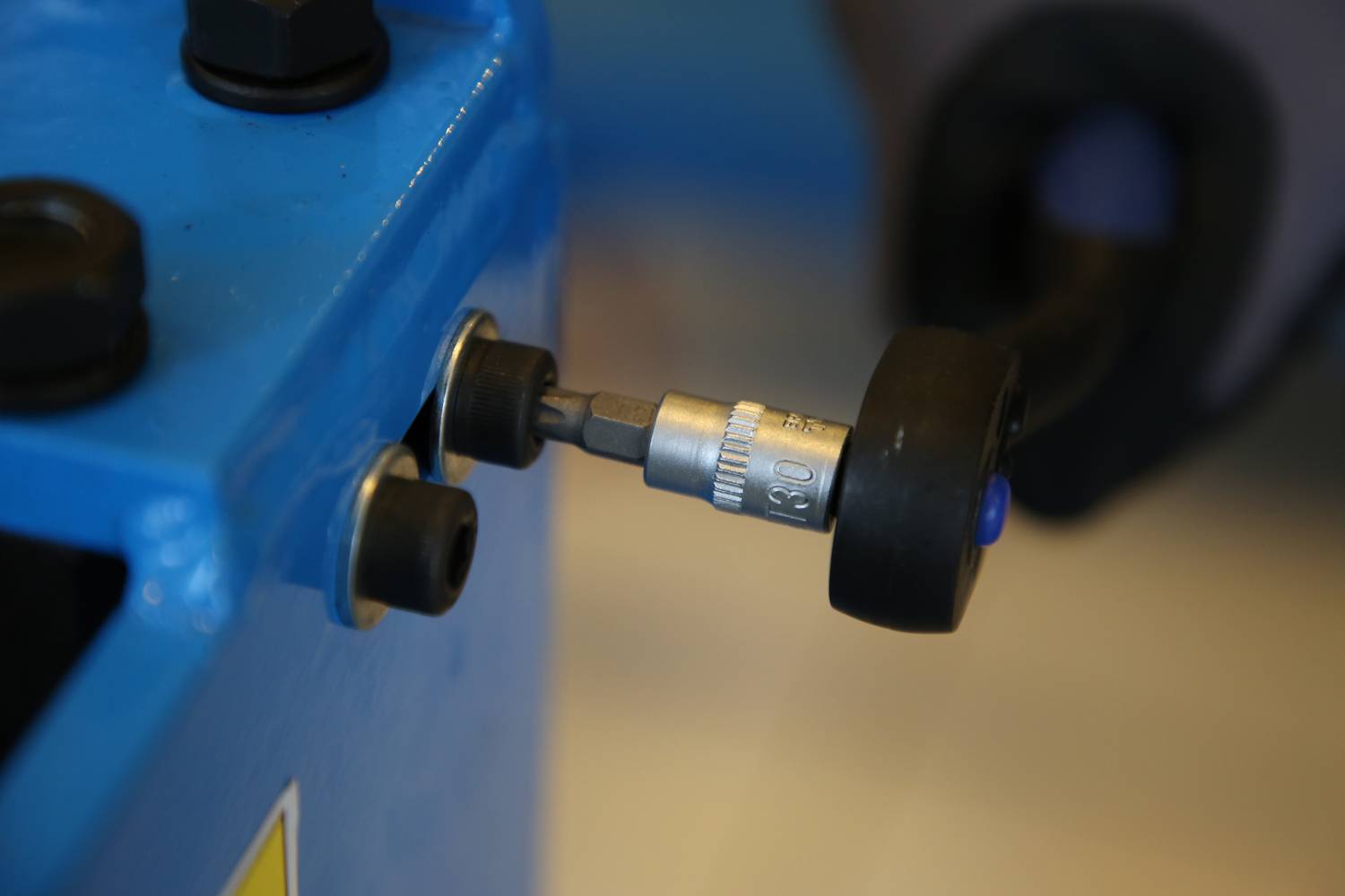 Ręcznie trzymany koniec narzędzia jest wsunięty w maszynę lub mechanizm, który jest zabarwiony na niebiesko.