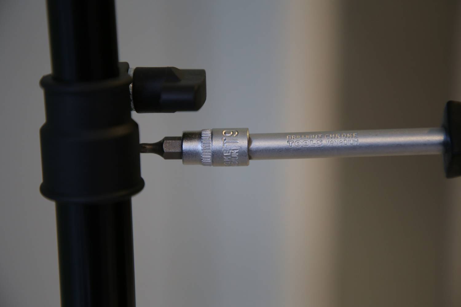 Fragment przedstawia statyw fotograficzny z wkręconym wkrętakiem, który jest używany do pracy przy śrubie.