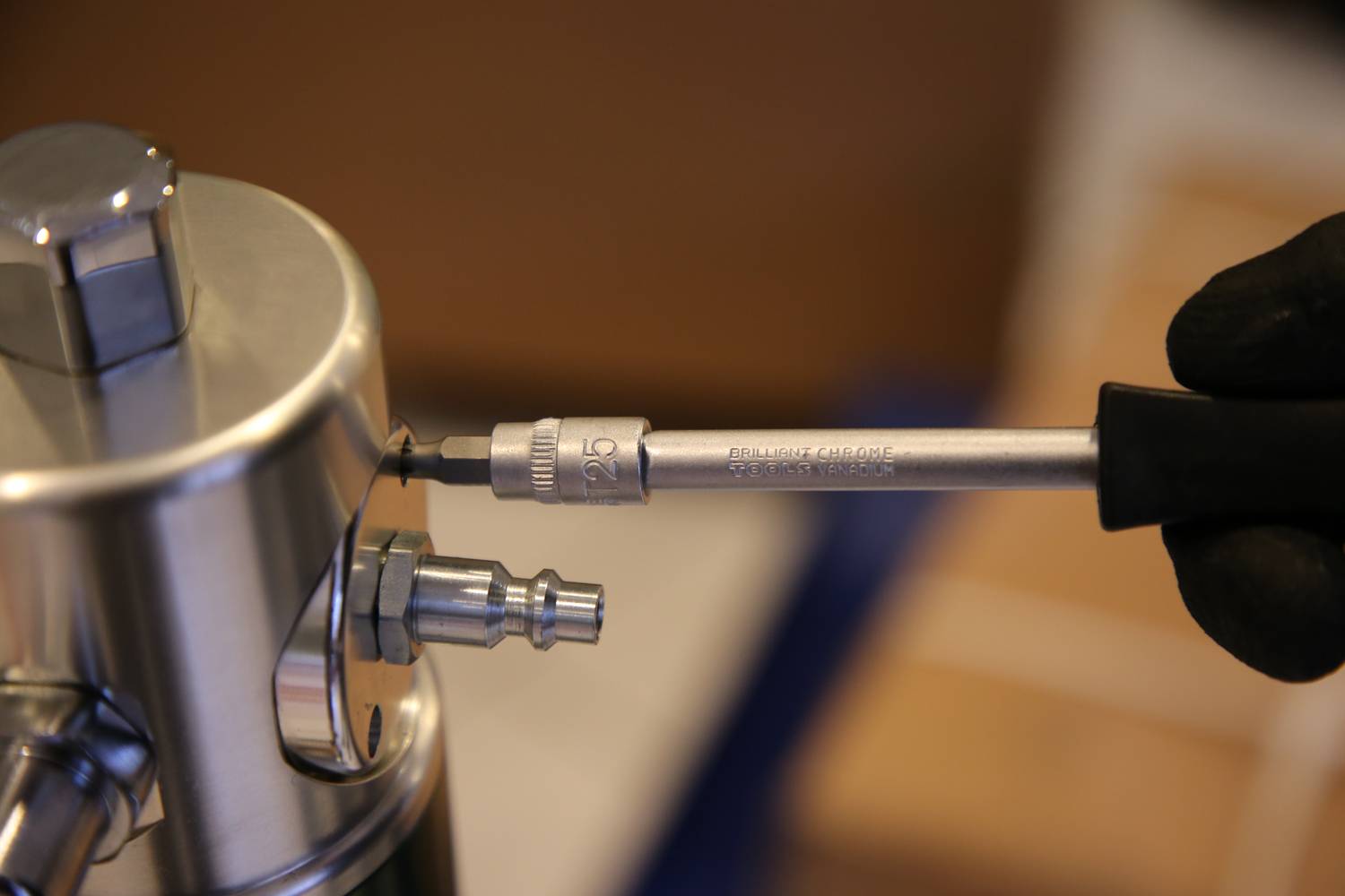 Dłoń używa klucza z grzechotką do zamocowania śruby w metalowym urządzeniu. Urządzenie posiada różne złącza.