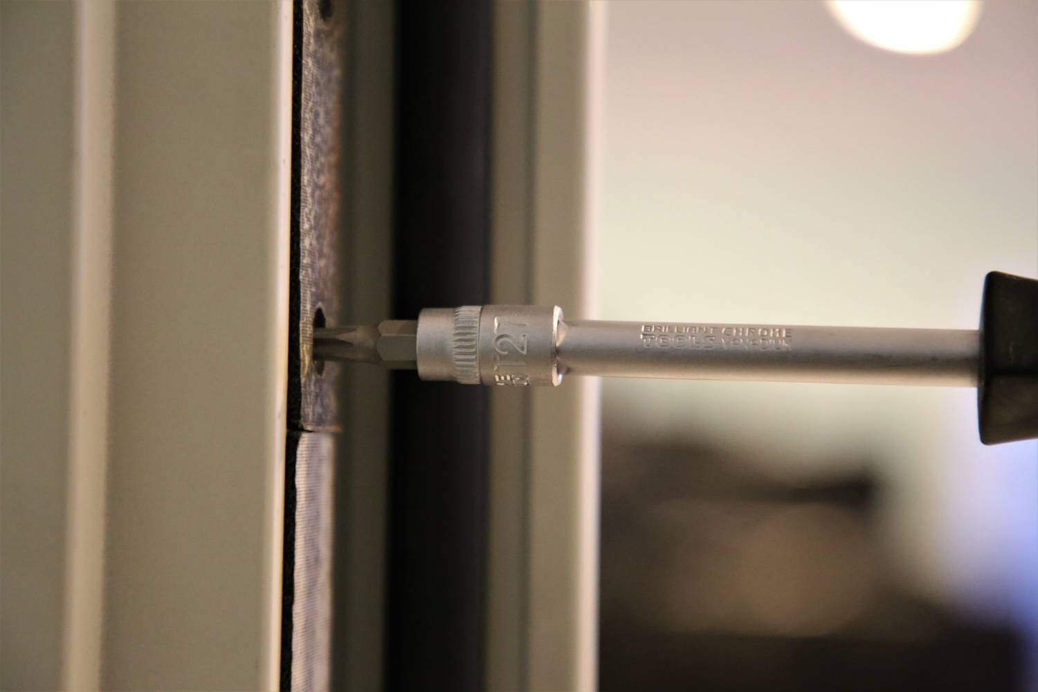 'Wkrętak jest wkręcany w śrubę w futrynie drzwi, prawdopodobnie podczas naprawy lub montażu.'