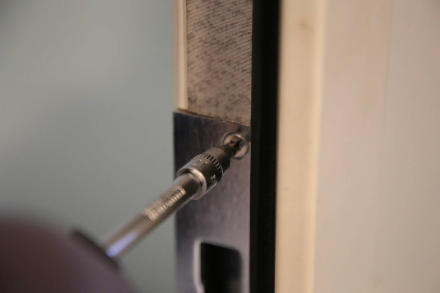 Zbliżenie śrubokrętu dokręcającego śrubę w zawiasie drzwiowym.