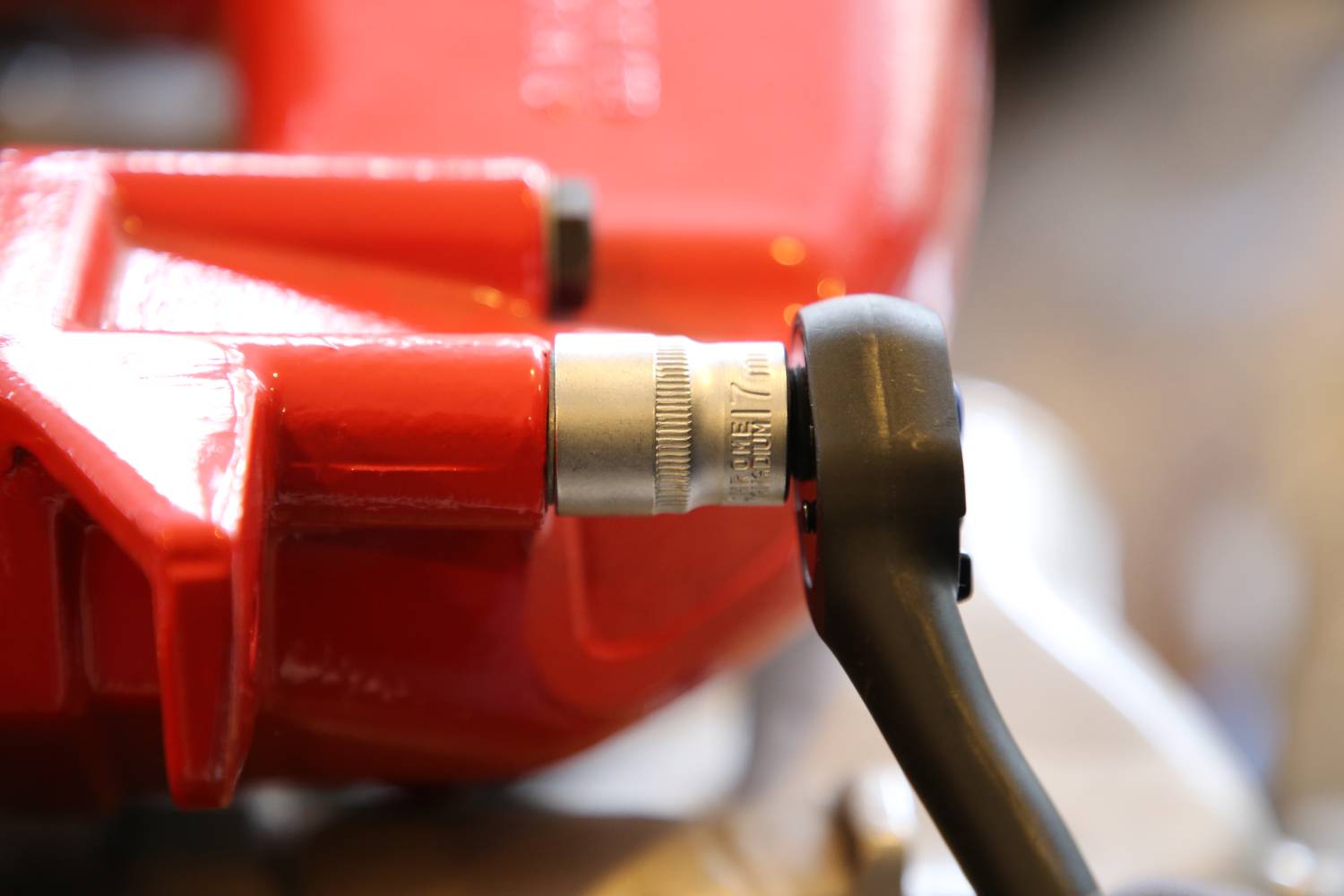 Zbliżenie czerwonego zacisku hamulcowego z czarnym kluczem dynamometrycznym przymocowanym do niego, wskazującym napięcie.