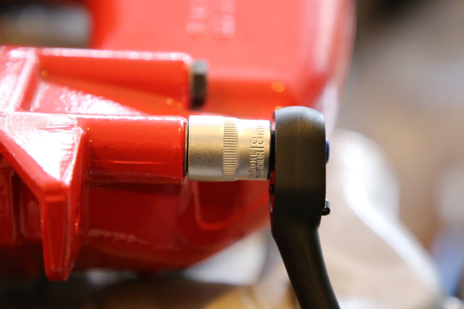 Zbliżenie czerwonego przedmiotu z srebrnym elementem metalowym i czarną dźwignią, prawdopodobnie będącego częścią narzędzia lub maszyny.