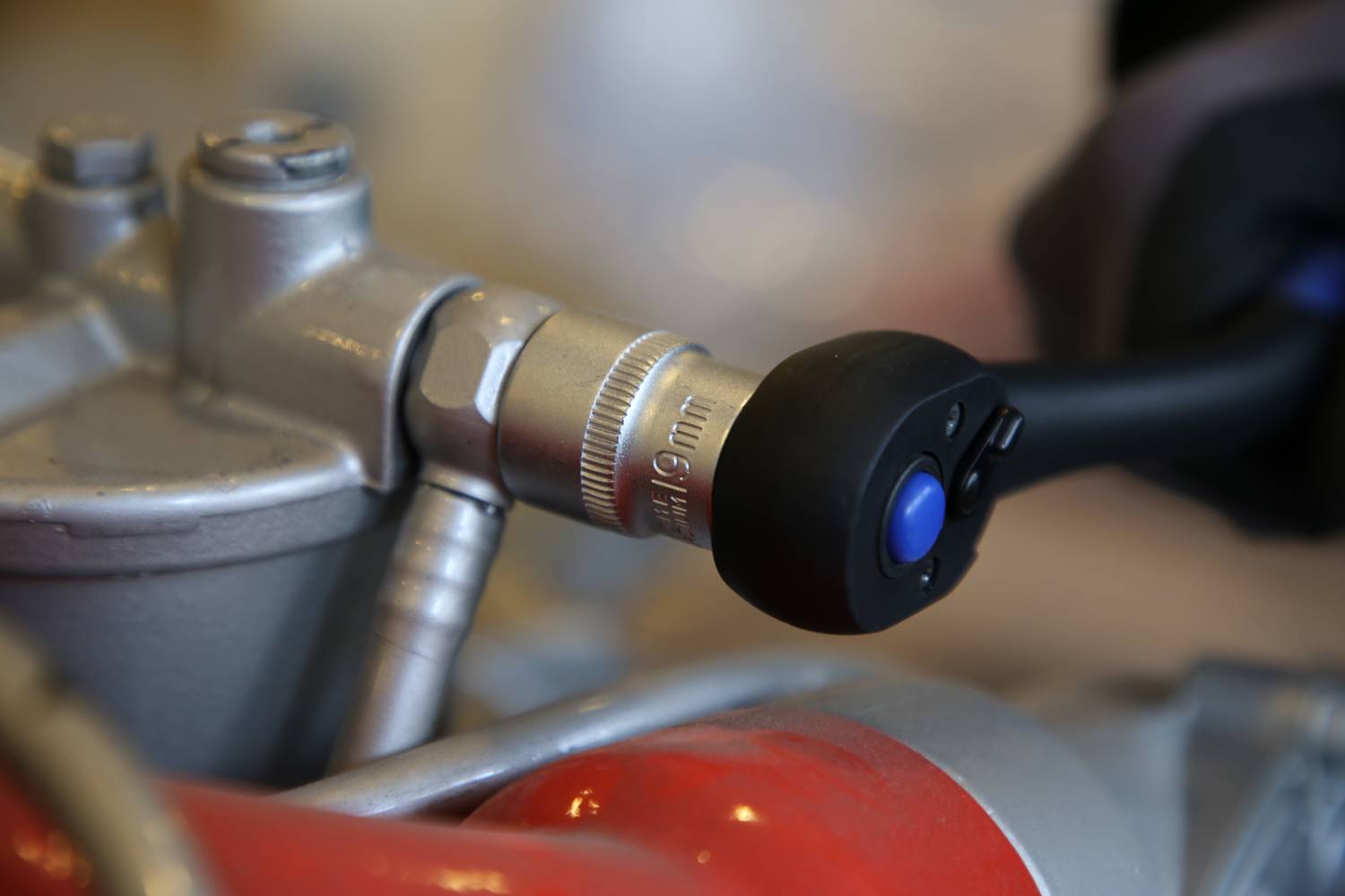 Zbliżenie narzędzia dokręcającego śrubę w elemencie motocykla kluczem dynamometrycznym. Ręce w rękawicach roboczych.