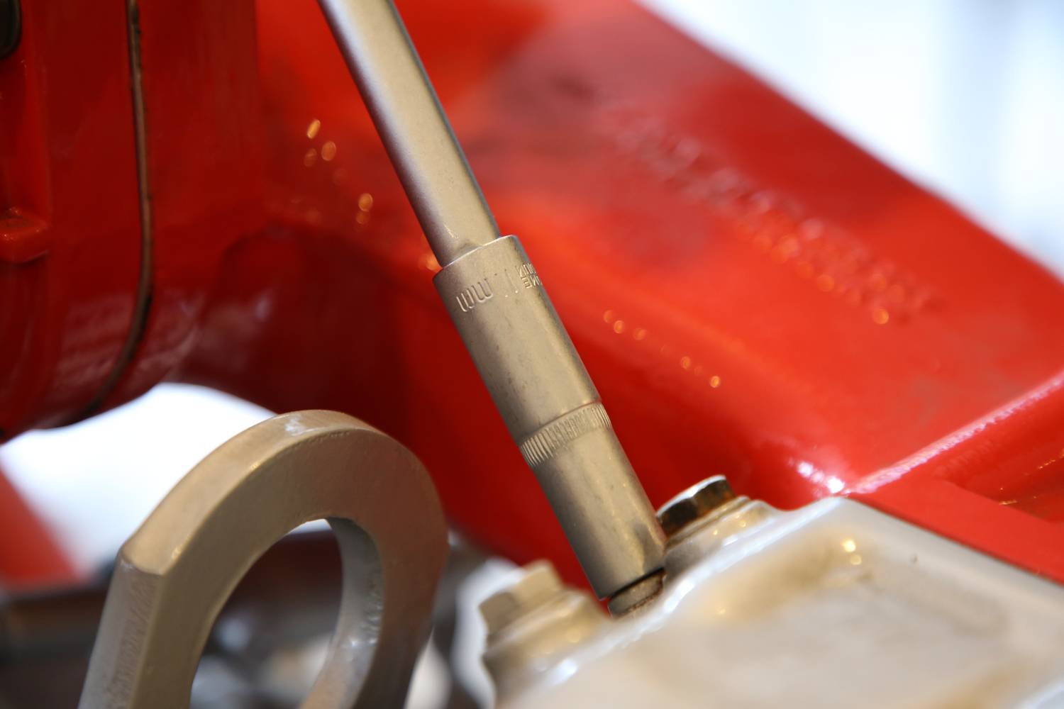 Srebrny klucz nastawny dokręca śrubę w czerwonym urządzeniu metalowym. Zbliżenie ukazuje szczegóły narzędzia.