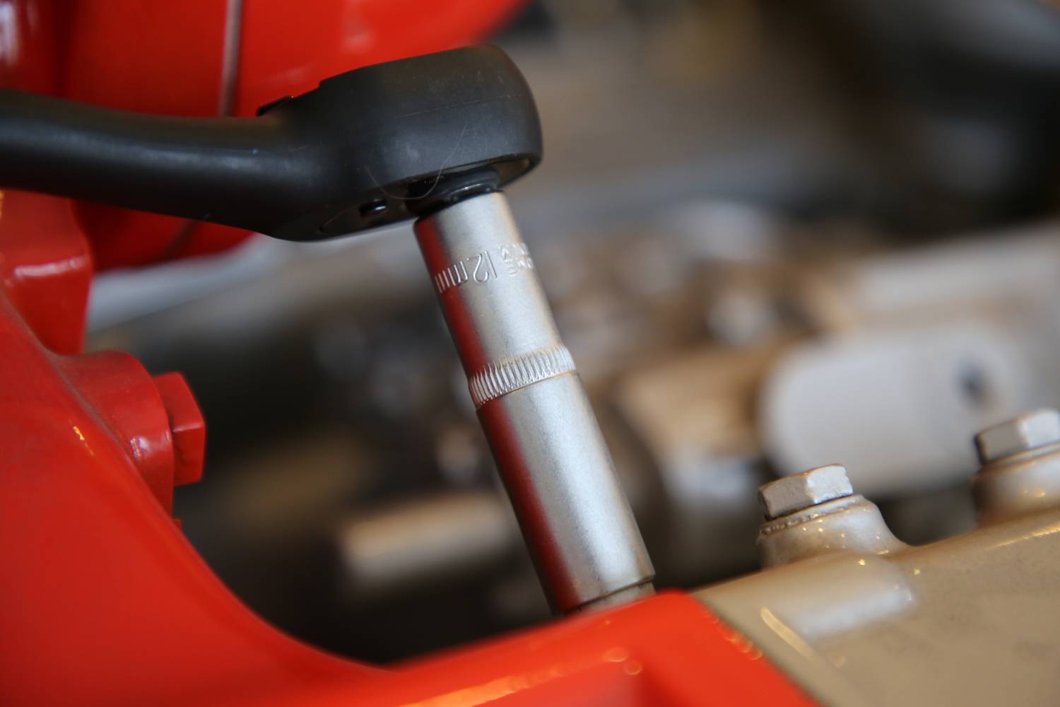 Zbliżenie narzędzia mocującego śrubę w silniku maszyny. Widoczne są czerwone i srebrne elementy.