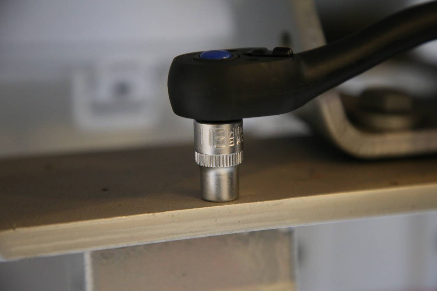 Zbliżenie klucza dynamometrycznego dokręcającego śrubę. Klucz jest czarny z niebieskim przyciskiem.