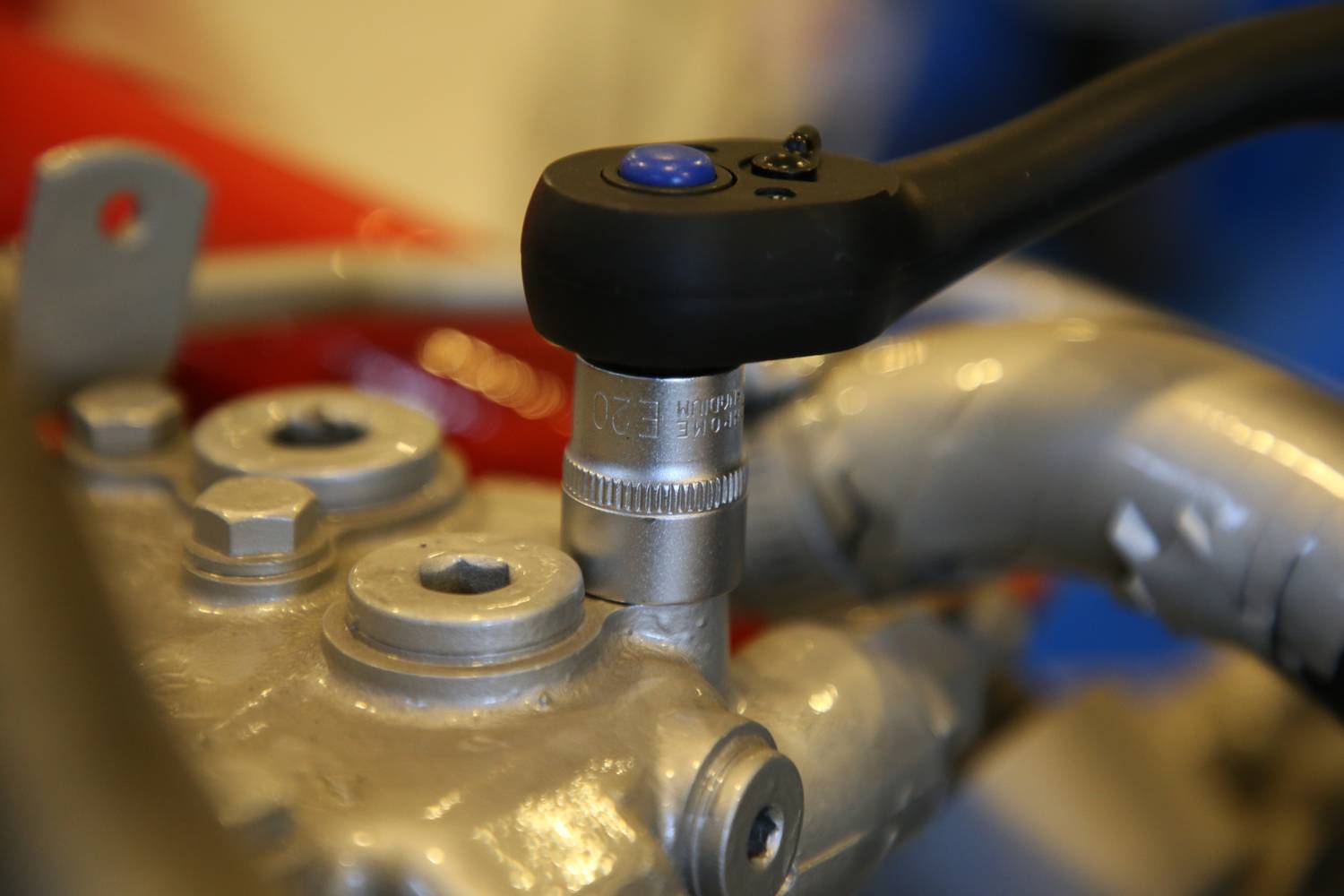 Grzechotka dokręca śrubę w metalowym elemencie. Scena ukazuje precyzyjną pracę rzemieślniczą w środowisku technicznym.