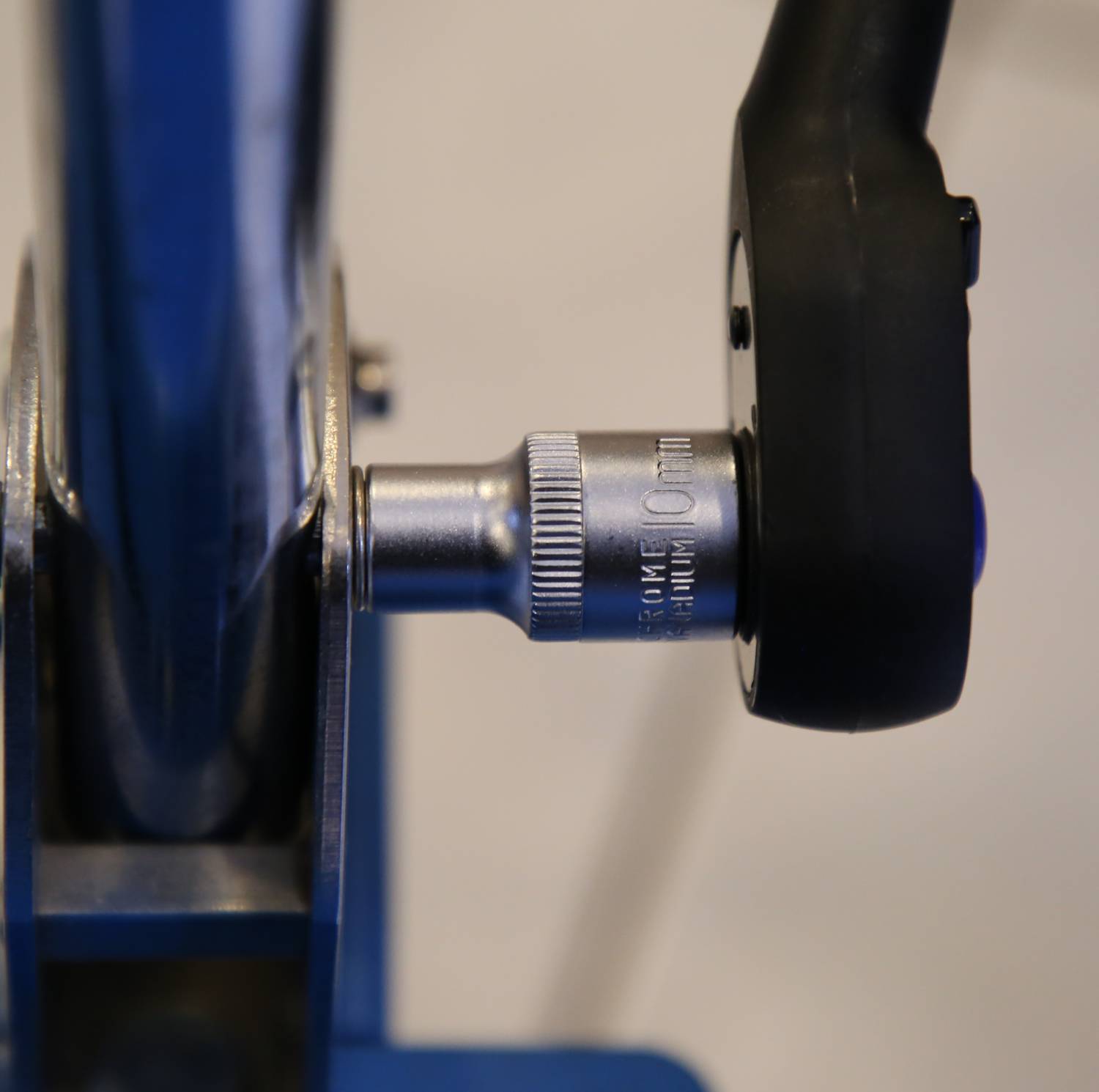 Zbliżenie srebrnego narzędzia ze skalą obok czarnej rękojeści, podłączonego do niebieskiego obiektu metalowego.