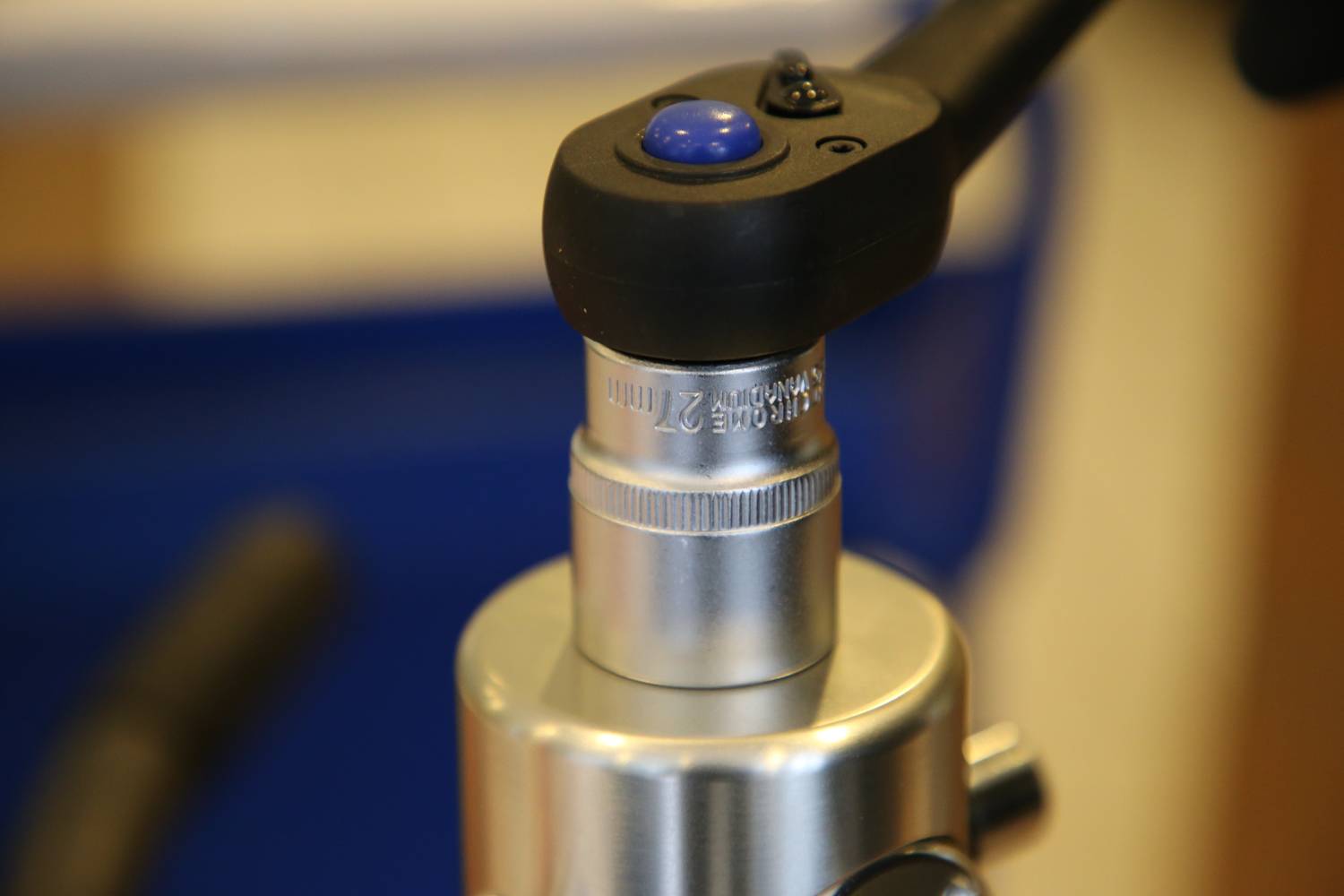 Zbliżenie obiektywu mikroskopowego, skupione na srebrnej soczewce z etykietą. Przymocowany jest do niej niebieskoczarny uchwyt.