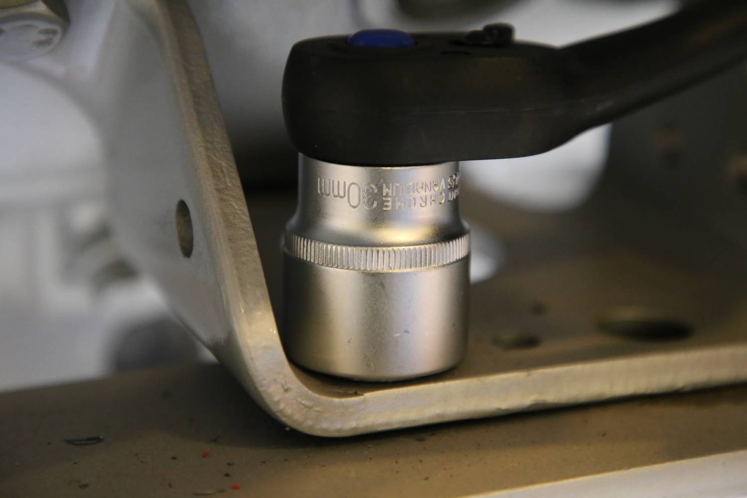 Klucz grzechotowy dokręca śrubę w metalowym urządzeniu. Scena przedstawia zbliżenie z naciskiem na narzędzie.