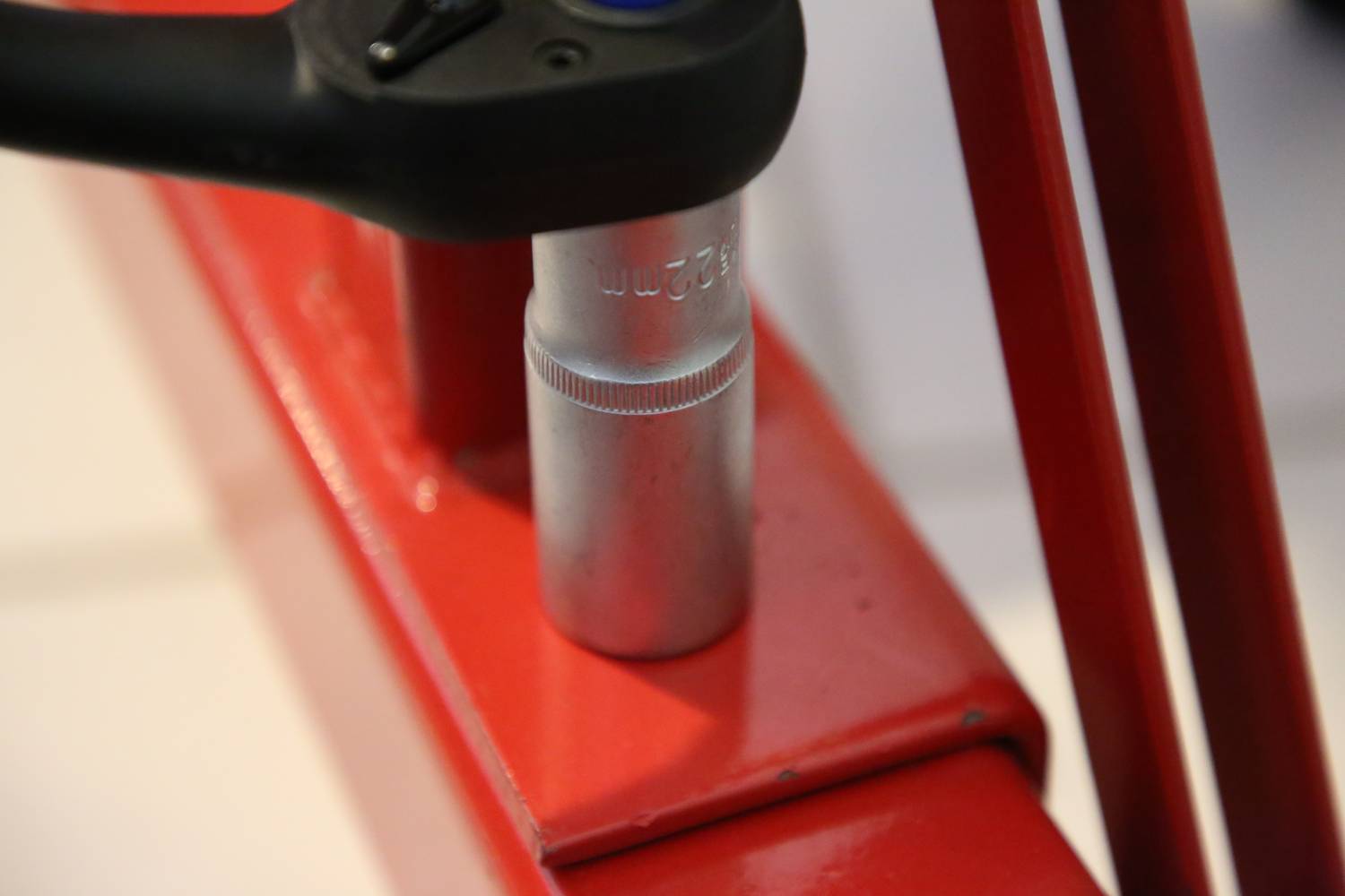 Zbliżenie klucza dokręcającego srebrną nakrętkę na czerwonym stojaku metalowym.