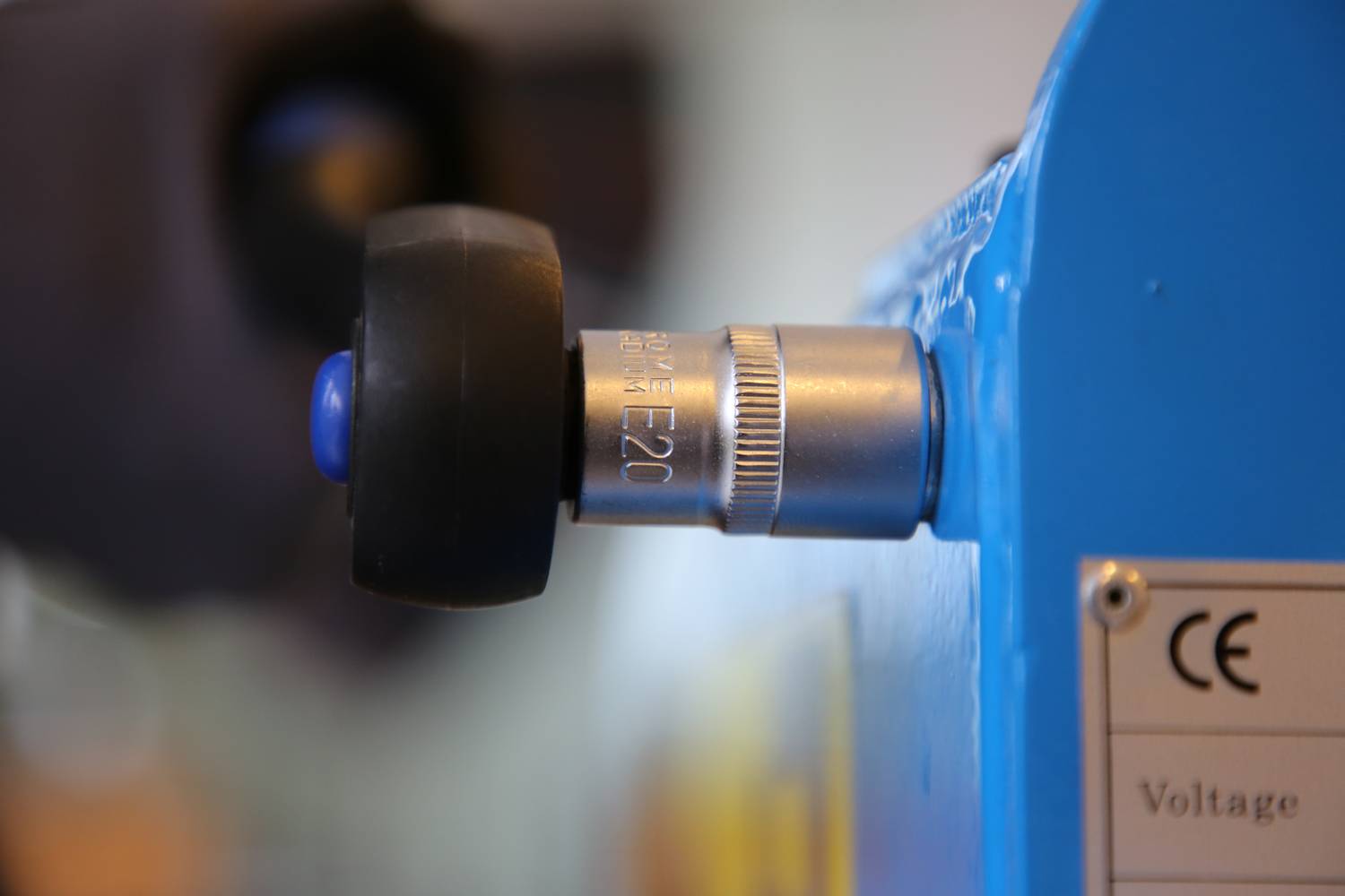 Srebrny pokrętło na niebieskim urządzeniu, oznaczone napisem 'E20'. Obok widoczna jest etykieta certyfikacji CE.