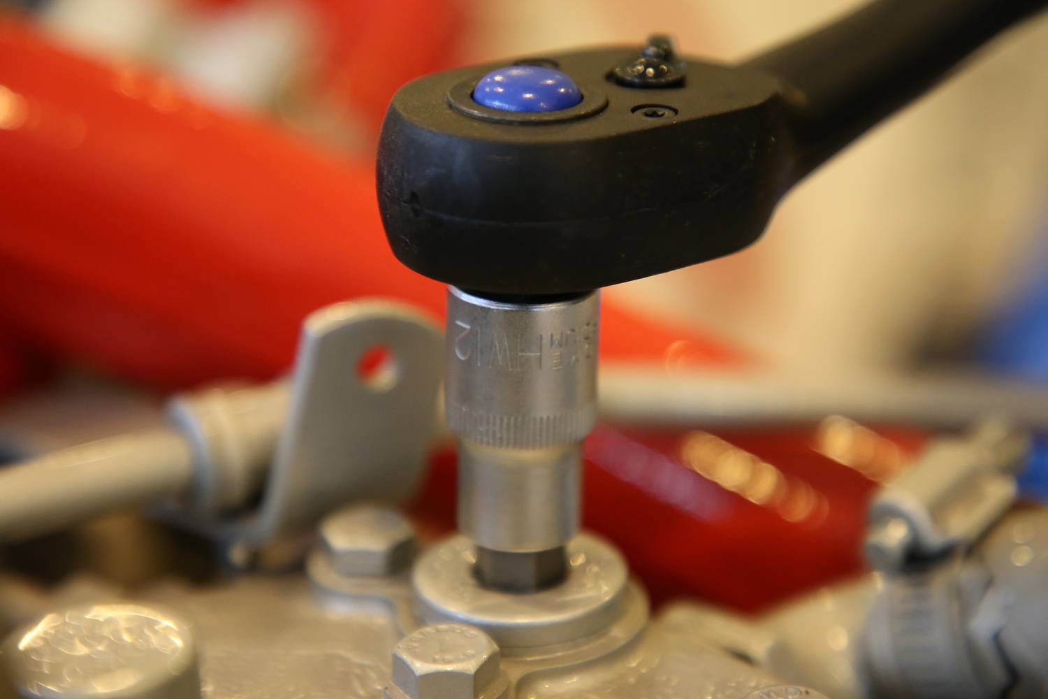 Zbliżenie klucza regulowanego pracującego na nakrętce. Na tle widoczne są czerwone przewody.